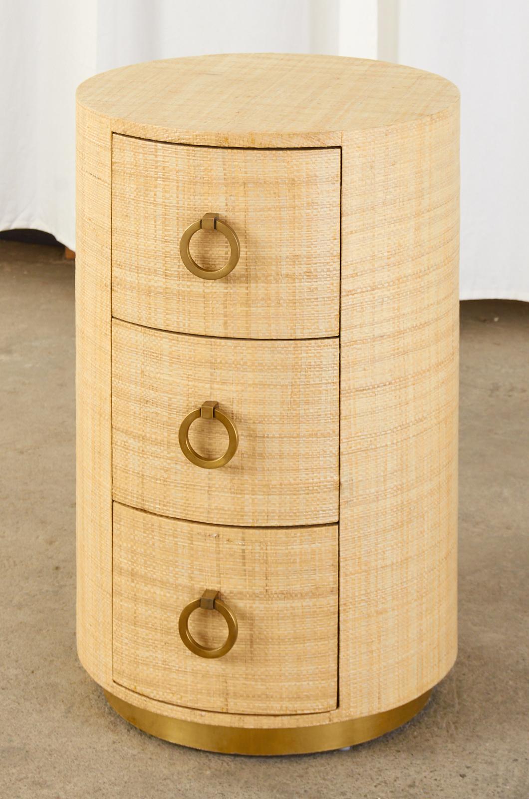 Chic circular nightstand or bed side table featuring an organic modern raffia grasscloth cladding or wrap. Made in the fabulous style and manner of Karl Springer. Crafted from radiant grained mahogany the circular column case has three storage
