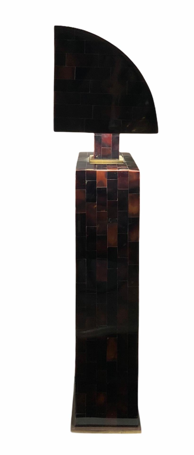 This is a sculptural wide heavy lamp shaped as a rectangular block in the lower part and as a ninety degree angle semi-tunnel in the upper part. Both parts are joined by a solid rectangular block. The whole sculpture is covered by small rectangular