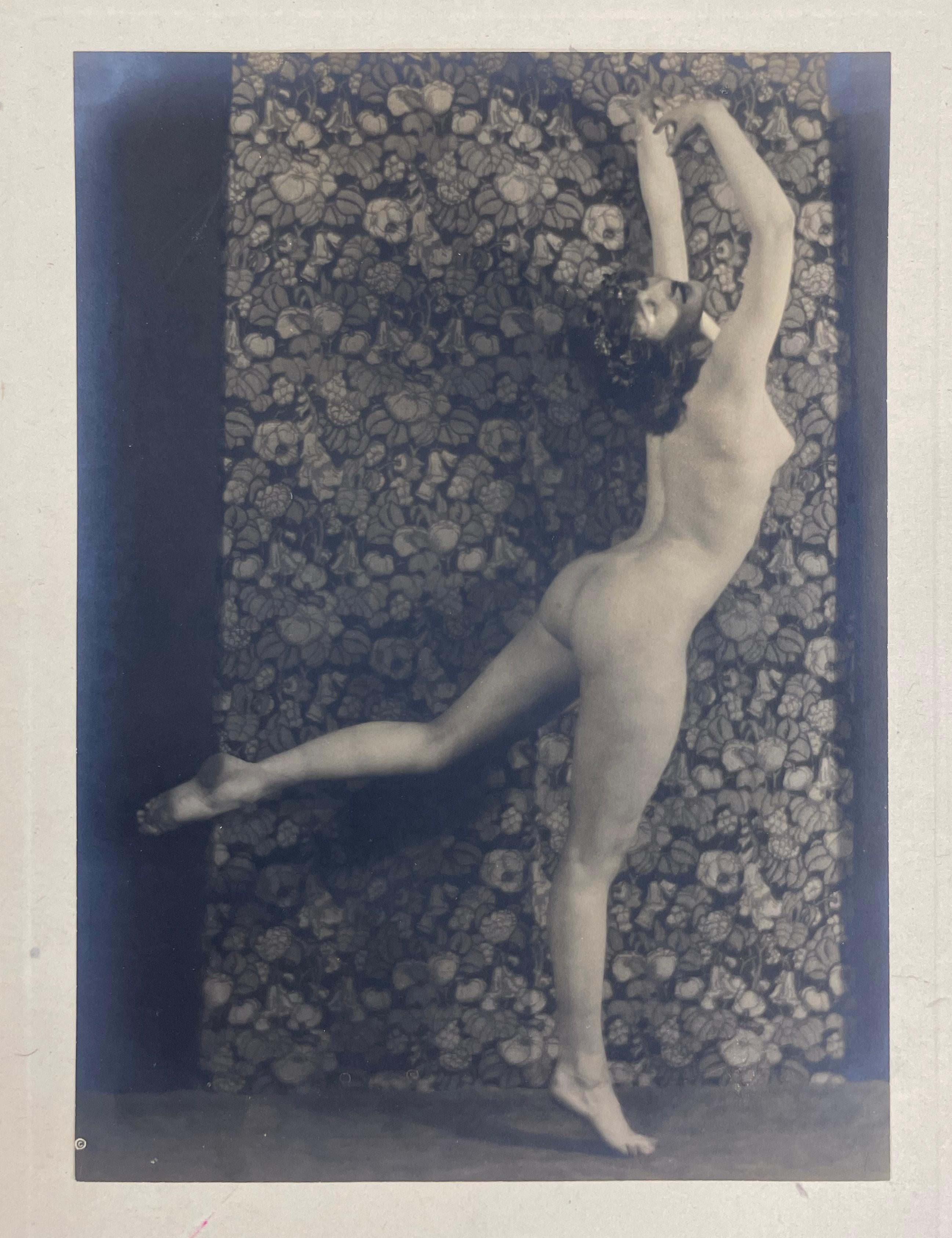 Nude Dancer, from The Female Figure series by Karl Struss features a nude woman standing on one leg, with her leg lifted in an arabesque position. Her arms are raised above her head as she arches back and turns her head towards the viewer. 

Nude