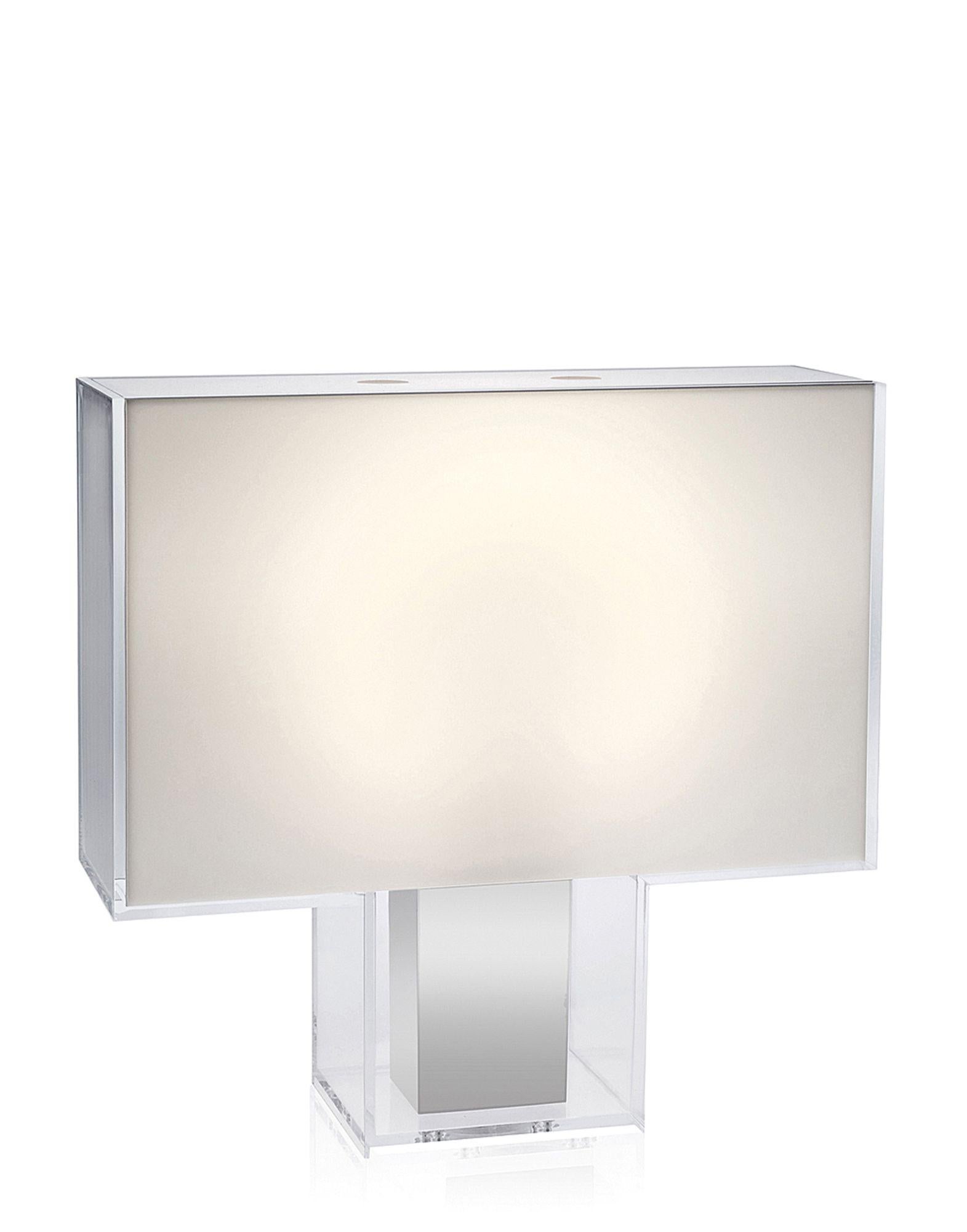 Rectangular table lamp featuring extremely clean lines vaguely reminiscent of an Art Deco mood. Tatì is unique because its external transparent PMMA case contains the lamp: a chrome base contains the diffuser and comes in either solid colour