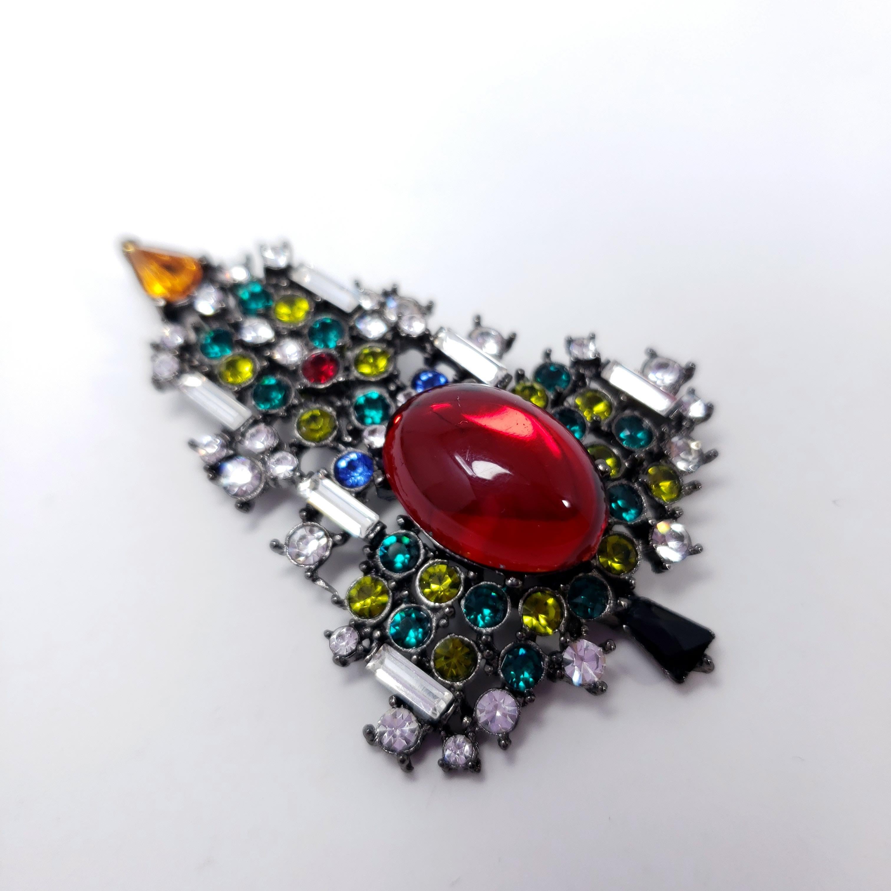 Festive Christmas / New Year pin brooch by Karu Arke Inc. This dazzling conifer is decorated with baguette and round cut crystals and a bold red ruby cabochon. Set on dark-gray gunmetal tone metal.

Vintage collector's costume jewelry pin,