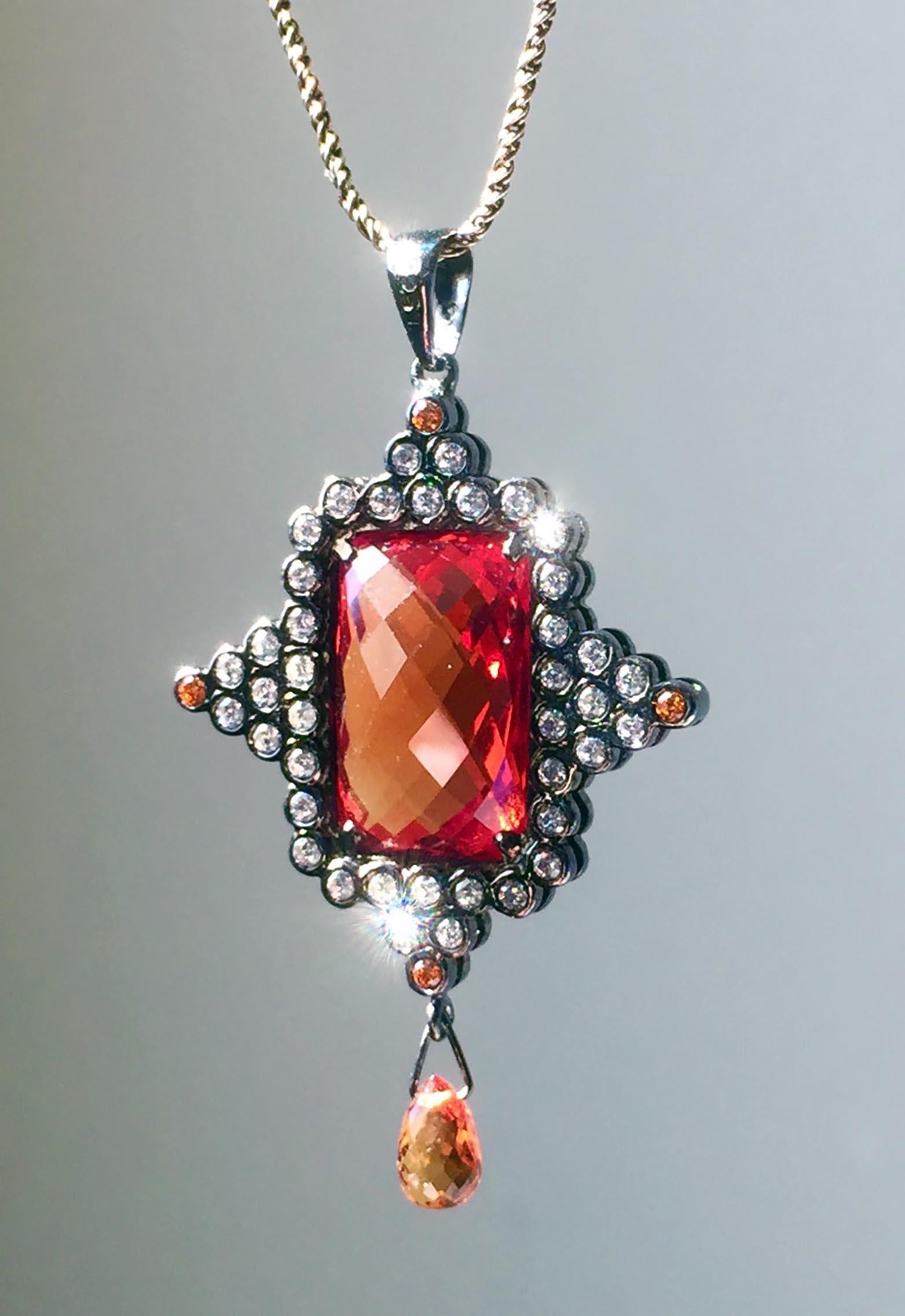 A Lovely Two Sided Sapphire Pendant is set in Blackened Silver and Features a Pillow/Checkerboard Cut Cultured Orange Sapphire of 13.8 Carats 16mm x 10mm x 6MM.Accented by another 5.8 Carats, 76 Pieces of Cultured White Sapphire Rounds and 8 Orange
