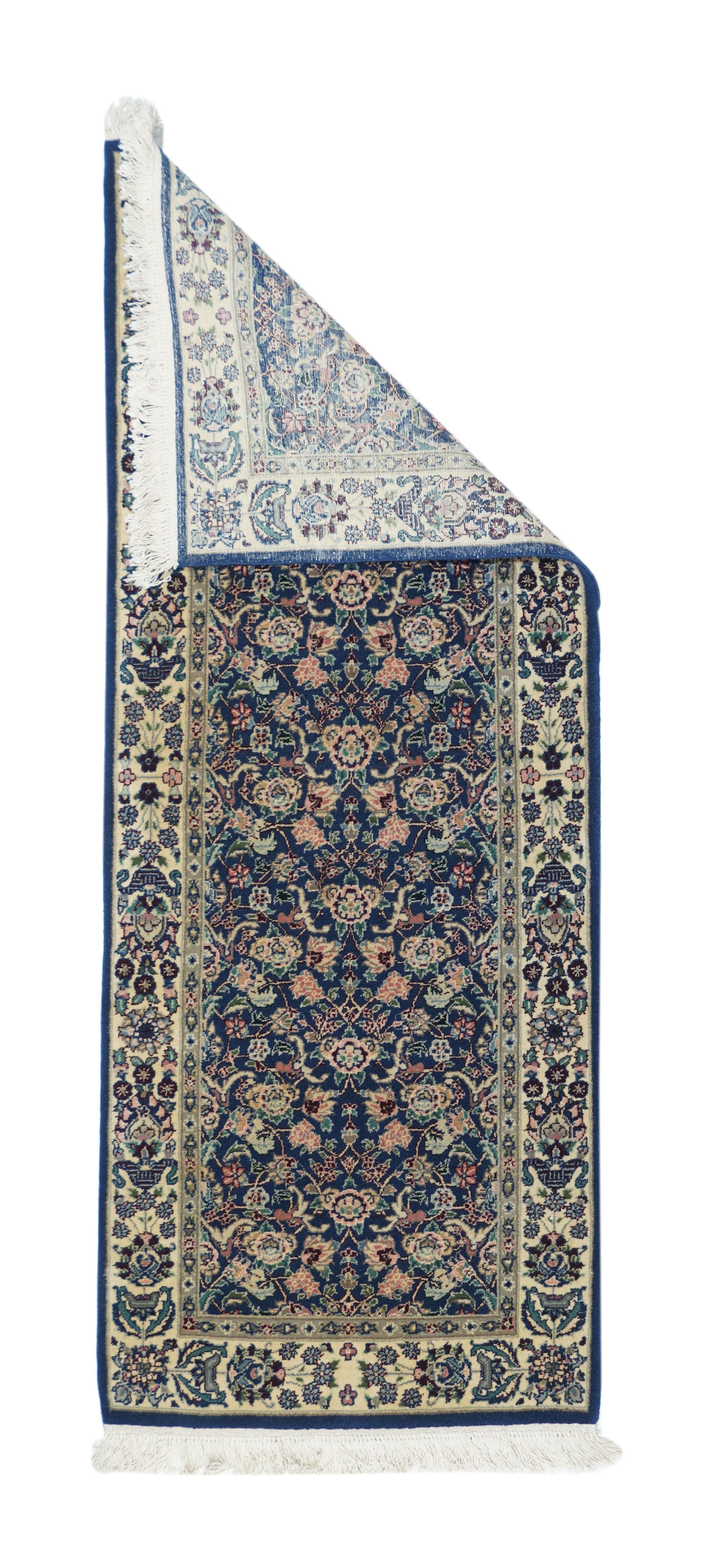 Alfombra Kashan 2'4'' x 6'0''. El campo azul marino presenta un estampado de rosas, rosetas, palmetas, florones y hojas de acanto, todo ello en tonos crema, rojo, salmón dorado, crudo, azul pálido y negro. Bordura de paja color crudo de palmetas de