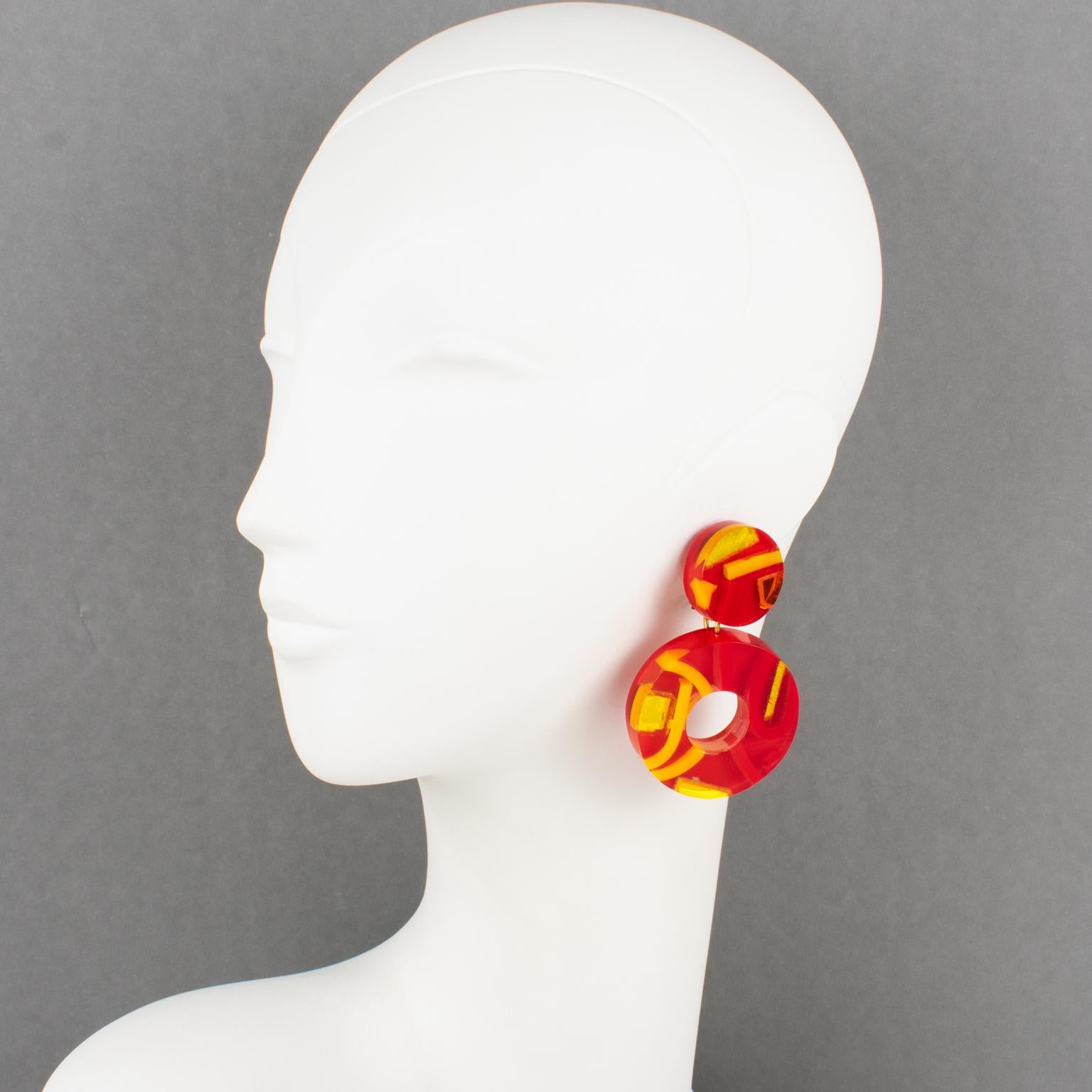 Harriet Bauknight designed those stunning lucite clip-on earrings for her brand Kaso in the 1980s. The massive donut dangling shape with a geometric design features dimensional multilayer Lucite elements with inclusions. The pieces boast a