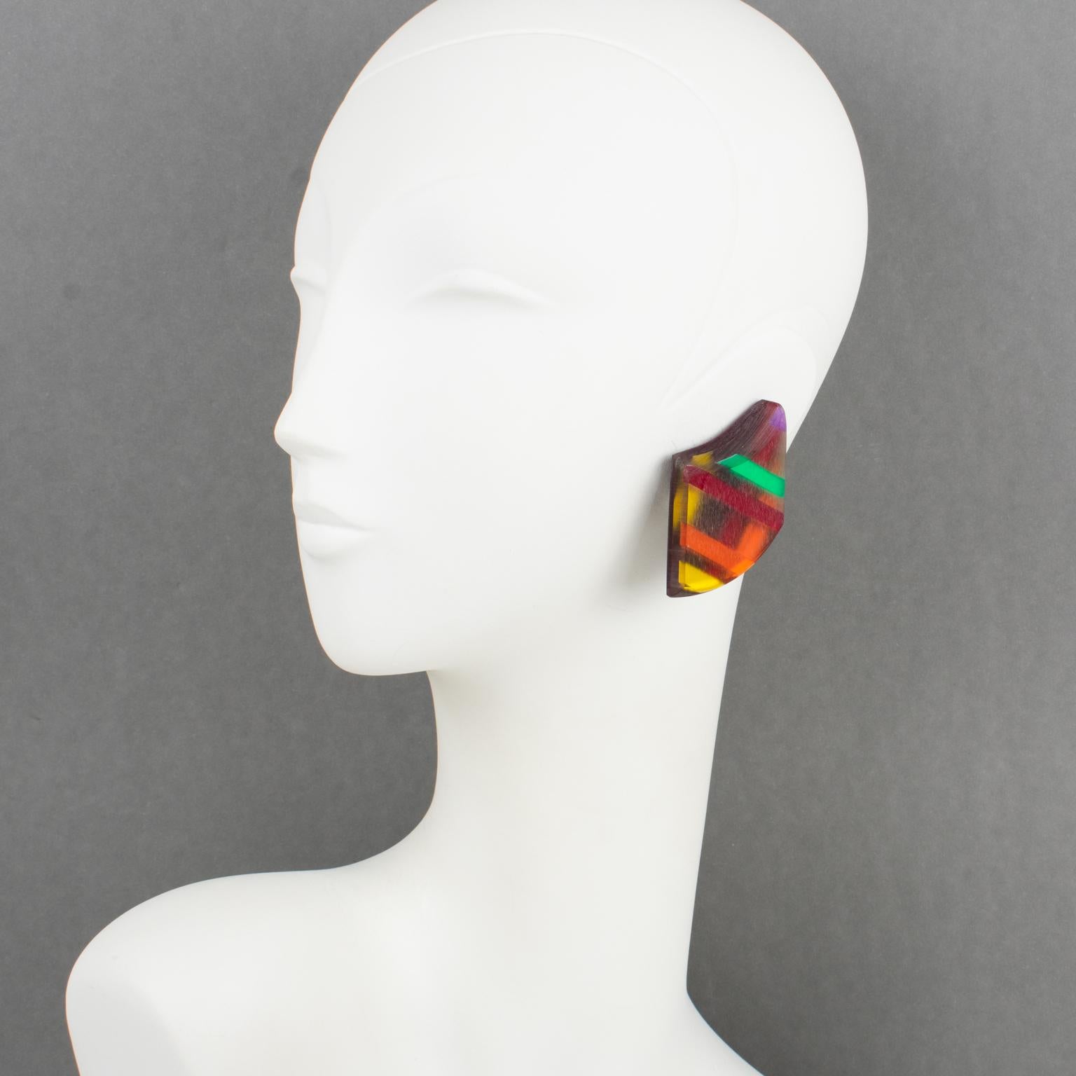 Harriet Bauknight for Kaso designed these colorful geometric Lucite clip-on earrings. They feature a massive asymmetric shape with a graphic design built with dimensional multilayers of Lucite and colorful harlequin inclusions and assorted bright