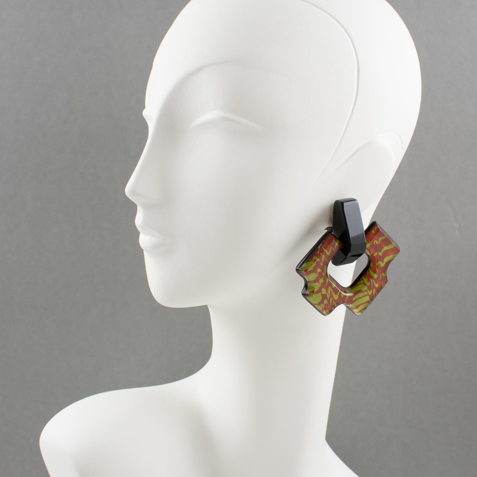 Harriet Bauknight designed these impressive Lucite clip-on earrings for her brand Kaso in the 1980s. The massive dangling shape features an asymmetric door-knocker in licorice black Lucite with colorful glitter effect inclusions. The inclusions
