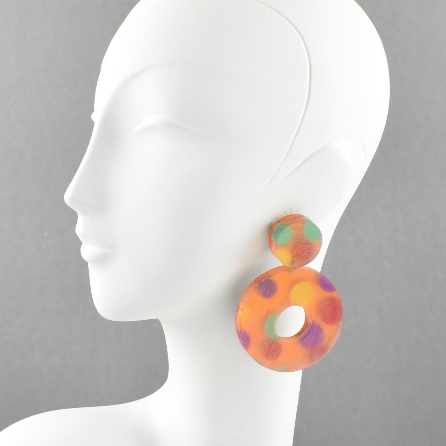 Spectacular oversized Lucite dangling clip-on earrings designed by Harriet Bauknight for Kaso. Large dangling shape with donut design featuring dimensional multilayers Lucite with colorful polka dot inclusions. Assorted bright colors of purple,