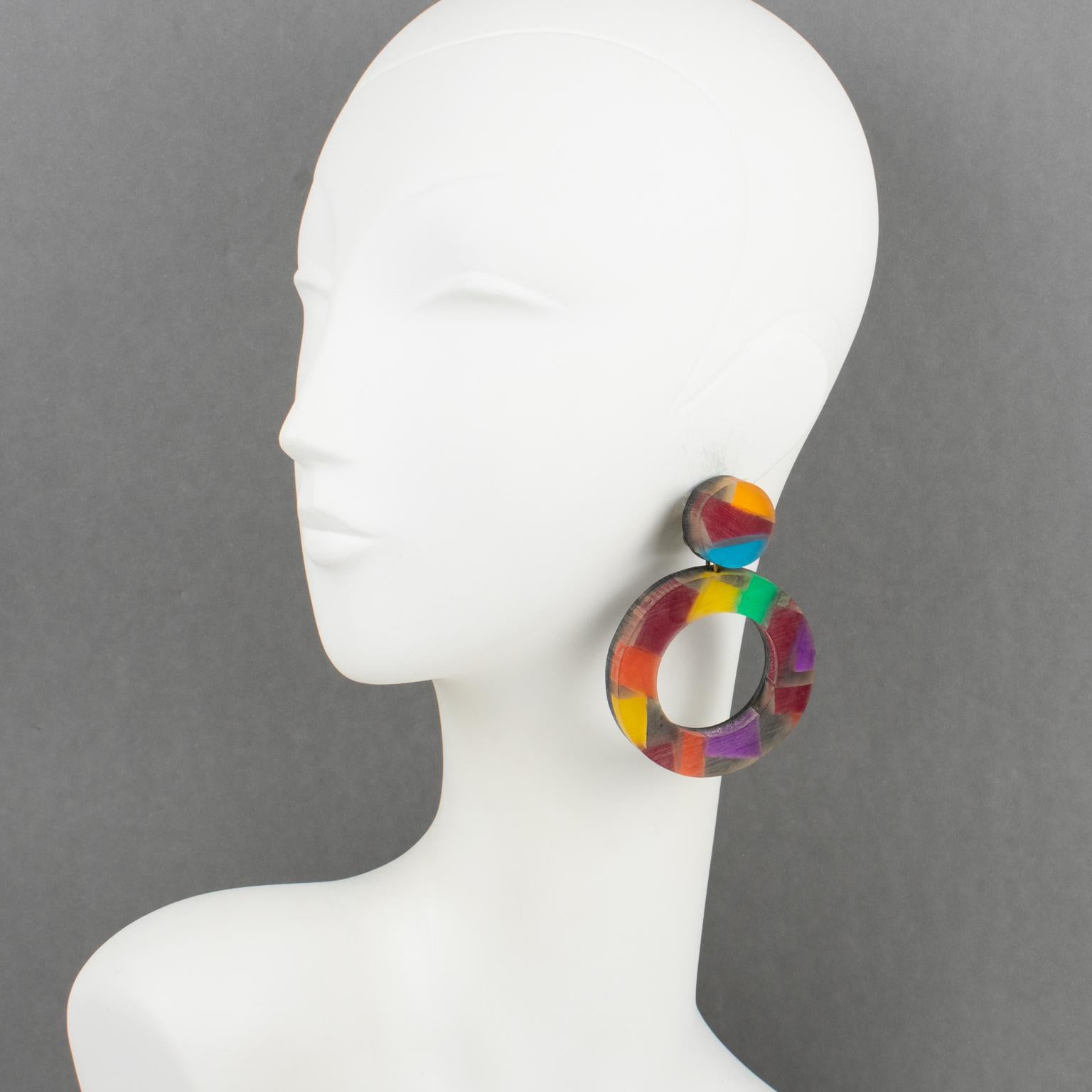 Harriet Bauknight for Kaso designed these stunning Lucite dangling clip-on earrings. They feature an oversized geometric donut shape with a dimensional multilayer black Lucite background with colorful harlequin pattern inclusions with a frosted