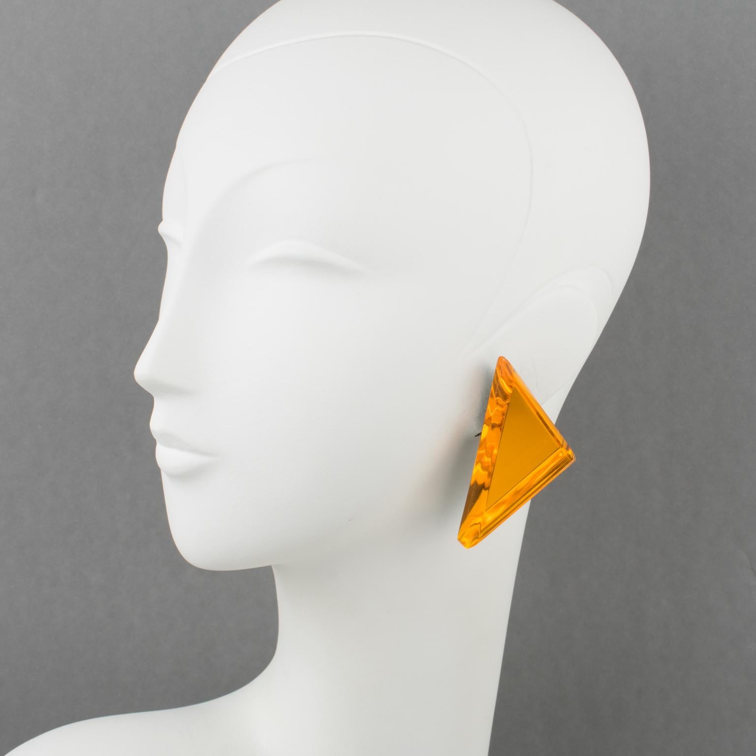 Beautiful oversized Lucite clip-on earrings designed by Harriet Bauknight for Kaso. A geometric triangle shape features a dimensional layer with a neon orange mirror-textured pattern and large beveling. The Kaso brand paper sticker was removed, but