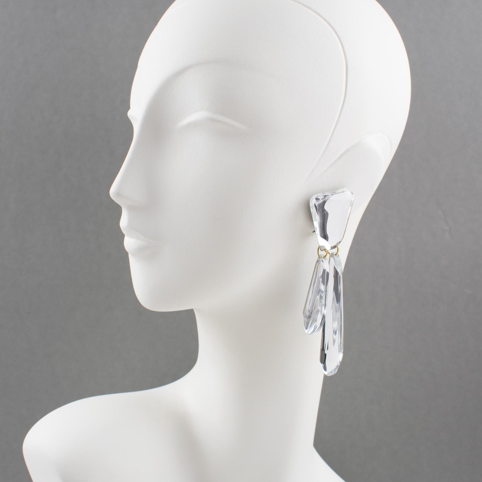 Harriet Bauknight for Kaso designed these elegant oversized dangling chandelier Lucite clip-on earrings. The dimensional geometric shape boasts dangling charms with a mirror-textured pattern and classy silver glitter color. The Kaso brand sticker