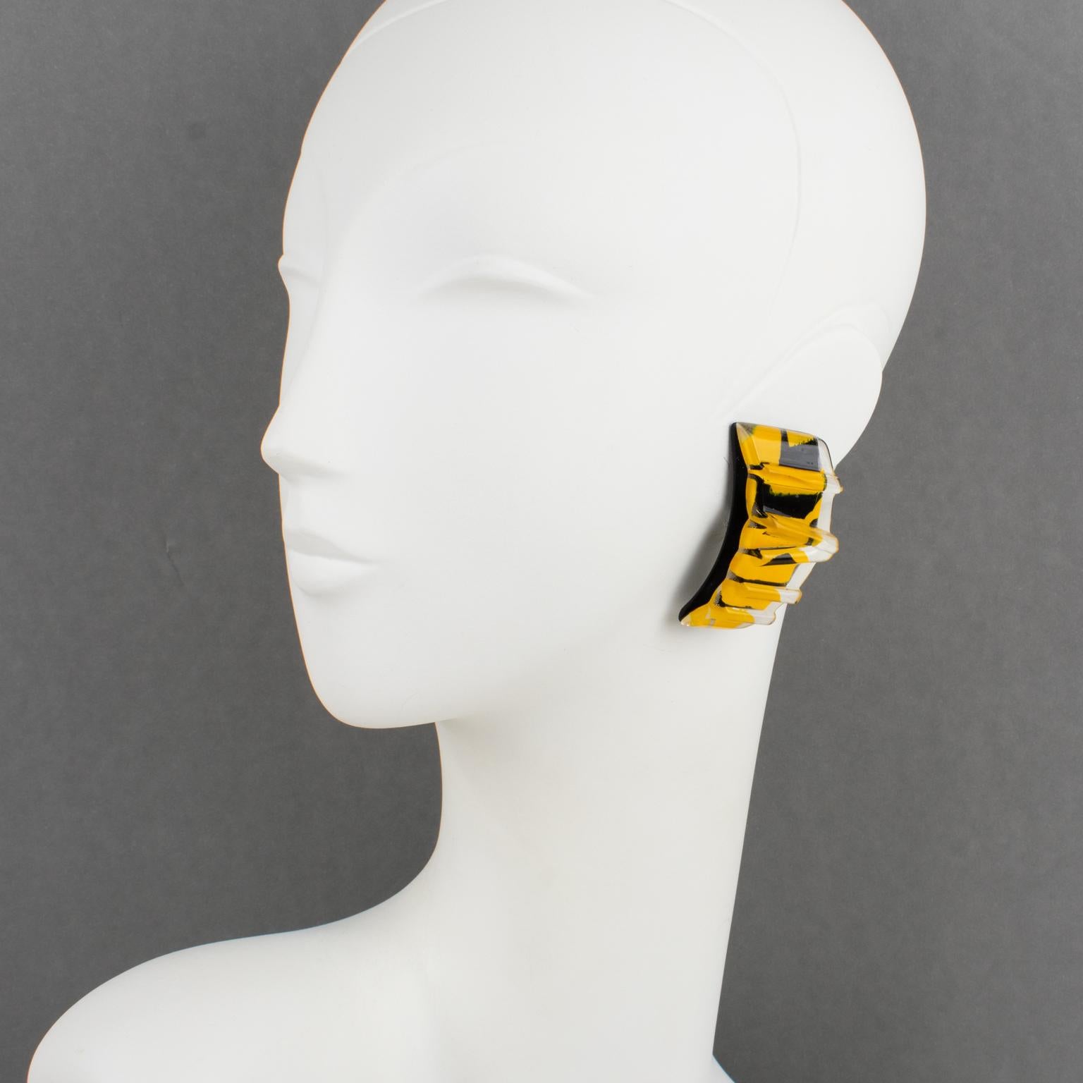 Harriet Bauknight designed these gorgeous Lucite clip-on earrings for her brand Kaso in the 1980s. The pieces feature a large dimensional elongated curved shape with a carved striped pattern design in black and yellow colors inclusions. The Kaso