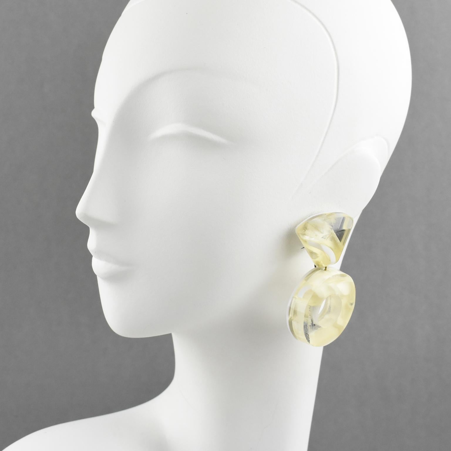 Harriet Bauknight for Kaso designed these stunning lucite clip-on earrings. The giant donut dangling shape with a geometric design features dimensional multilayer Lucite with inclusions. The pieces have a contrasted pattern in a mirror effect, a