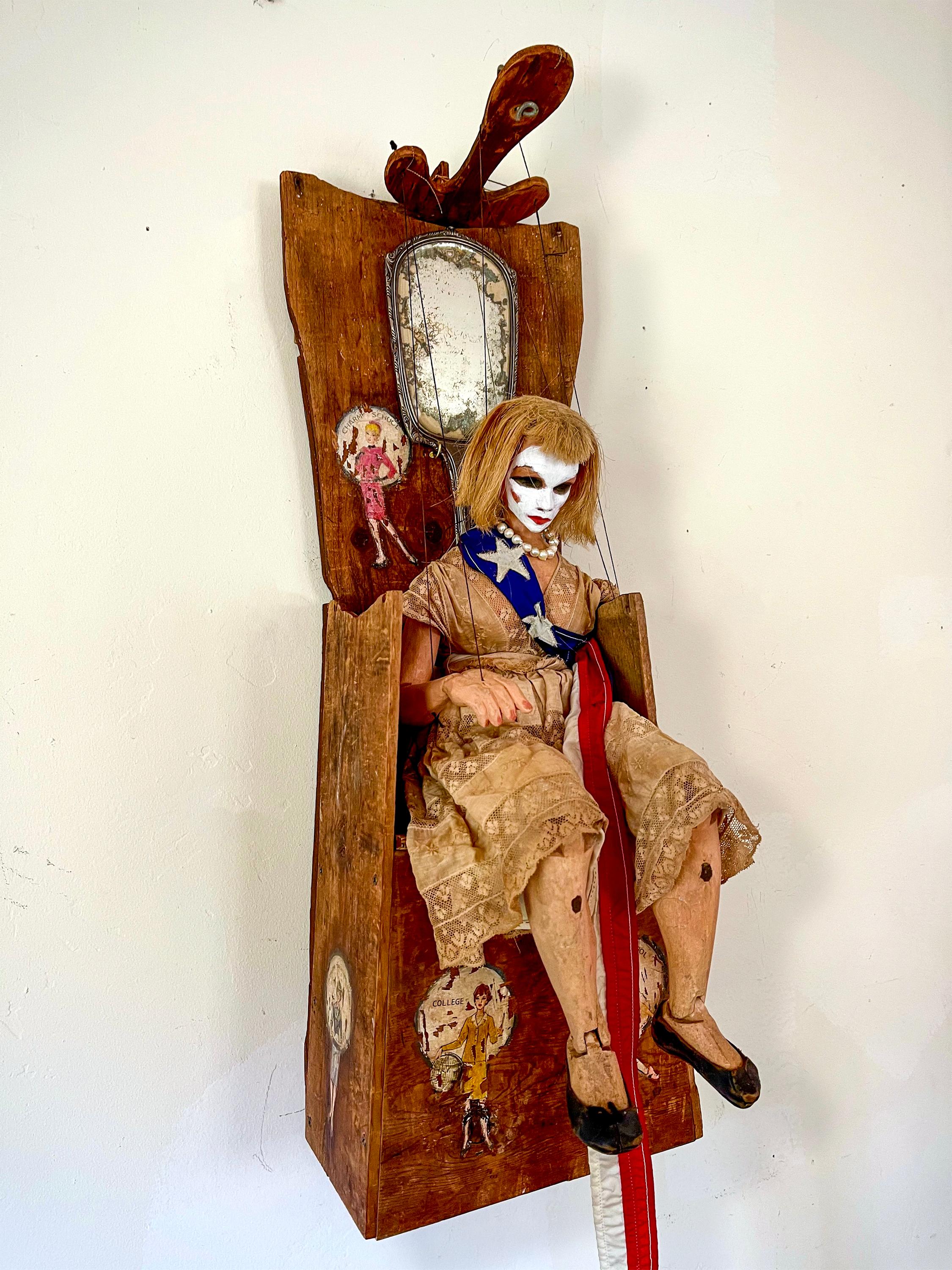assemblage sculpture: Handmade old wood throne, hand carved wood puppet in old dress and boat flag sash, real pearls, vintage Rolex watch, probably fake, vintage painted pictures girls' career game pieces, handmade wood controller, antique sterling