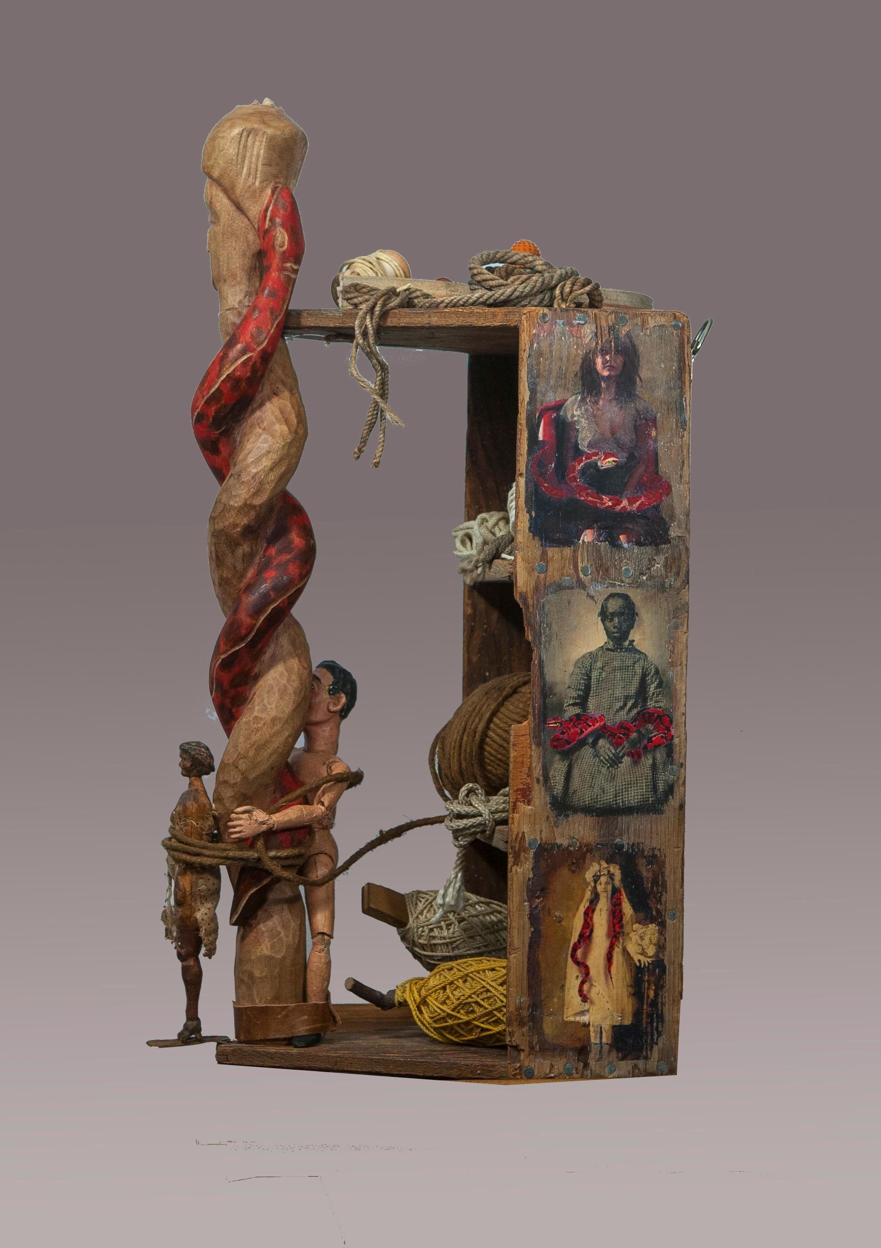 assemblage sculpture: Hand carved wood woman tied to hand carved staff of woman with snake used as handle of old wood toolbox, old rolls of string, twine & rope, hand made wood & gesso articulated man, hand painted digitally manipulated photos on