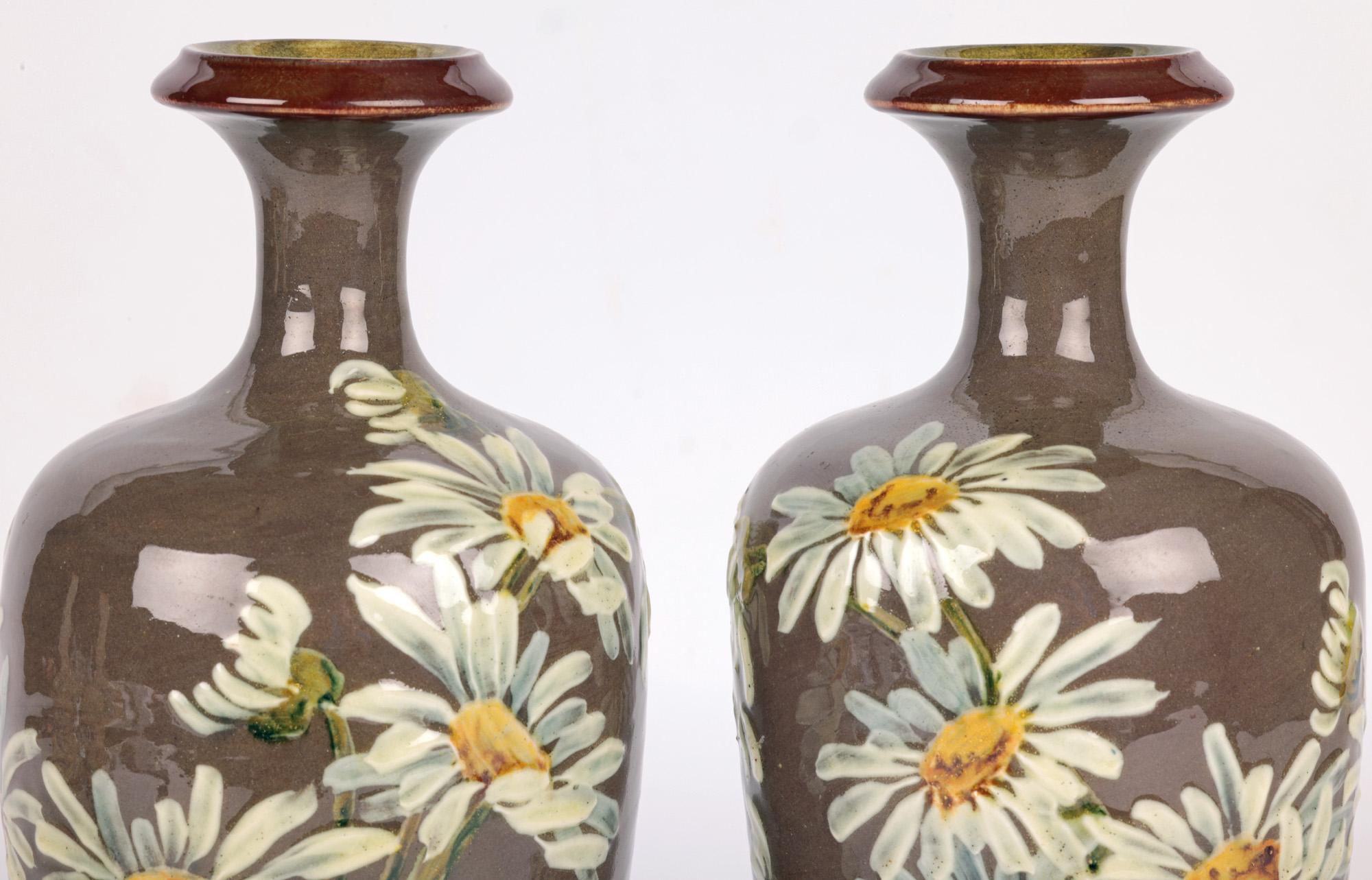 A stunning and fine pair Doulton Lambeth Impasto daisy painted vases by renowned Faience artist Kate Rogers and dated 1885. 

The stoneware vases are of tall bulbous shape standing raised on inverted bowl shaped bases with a tall tapering bulbous