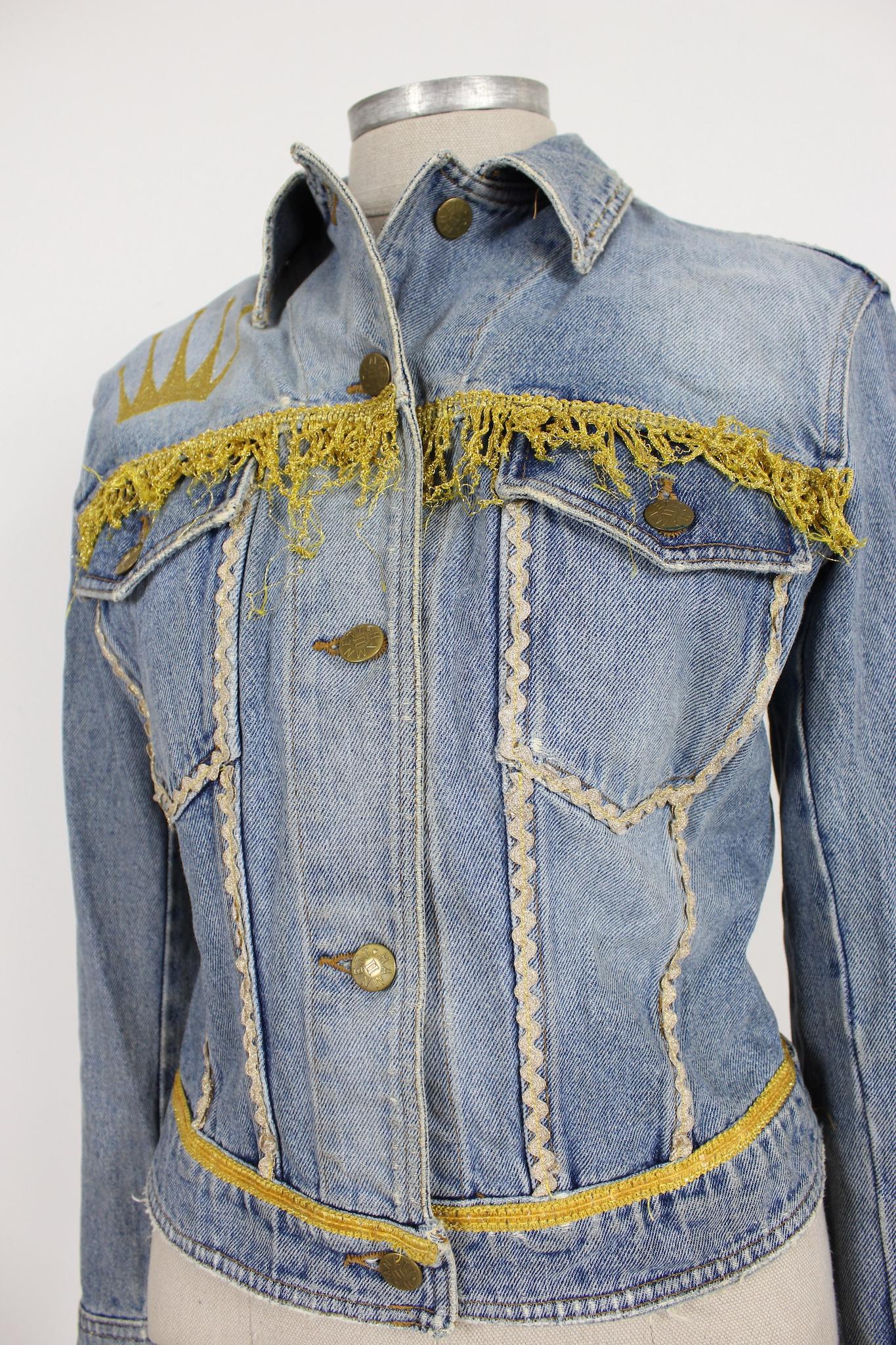 Stand out from the crowd in this unique 90s vintage Katharine Hamnett jeans jacket. Featuring golden fringes and a stitched golden crown, this jacket is a statement piece that will elevate any outfit. The size S fits perfectly and the denim material
