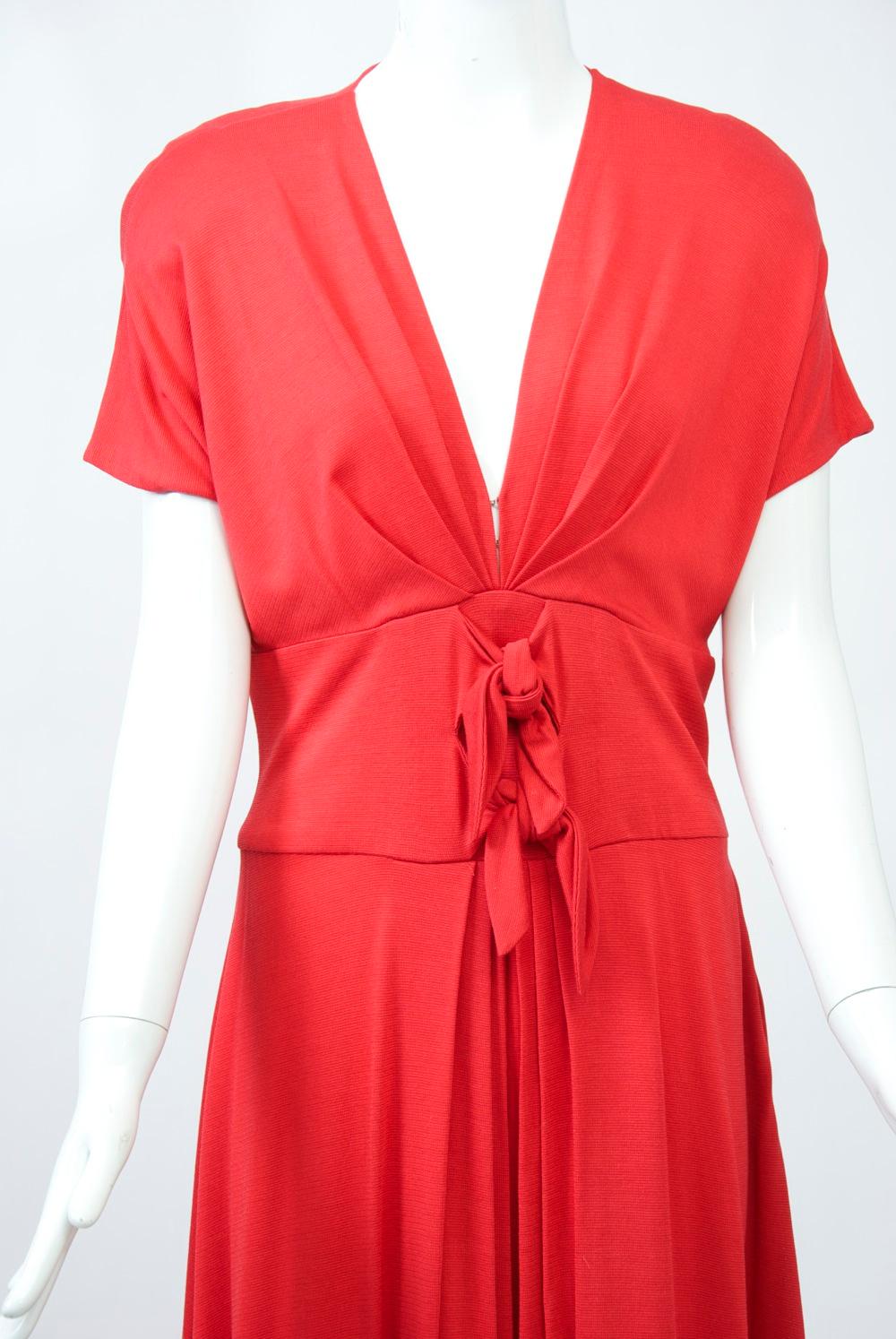 Kathryn Dianos long red dress in a rayon and nylon blend fabric featuring a set-in midriff with two ties, a deepv neckline and raglan cap sleeves. The bodice has tucked pleats at the V, which complement the inverted pleats below the midriff in