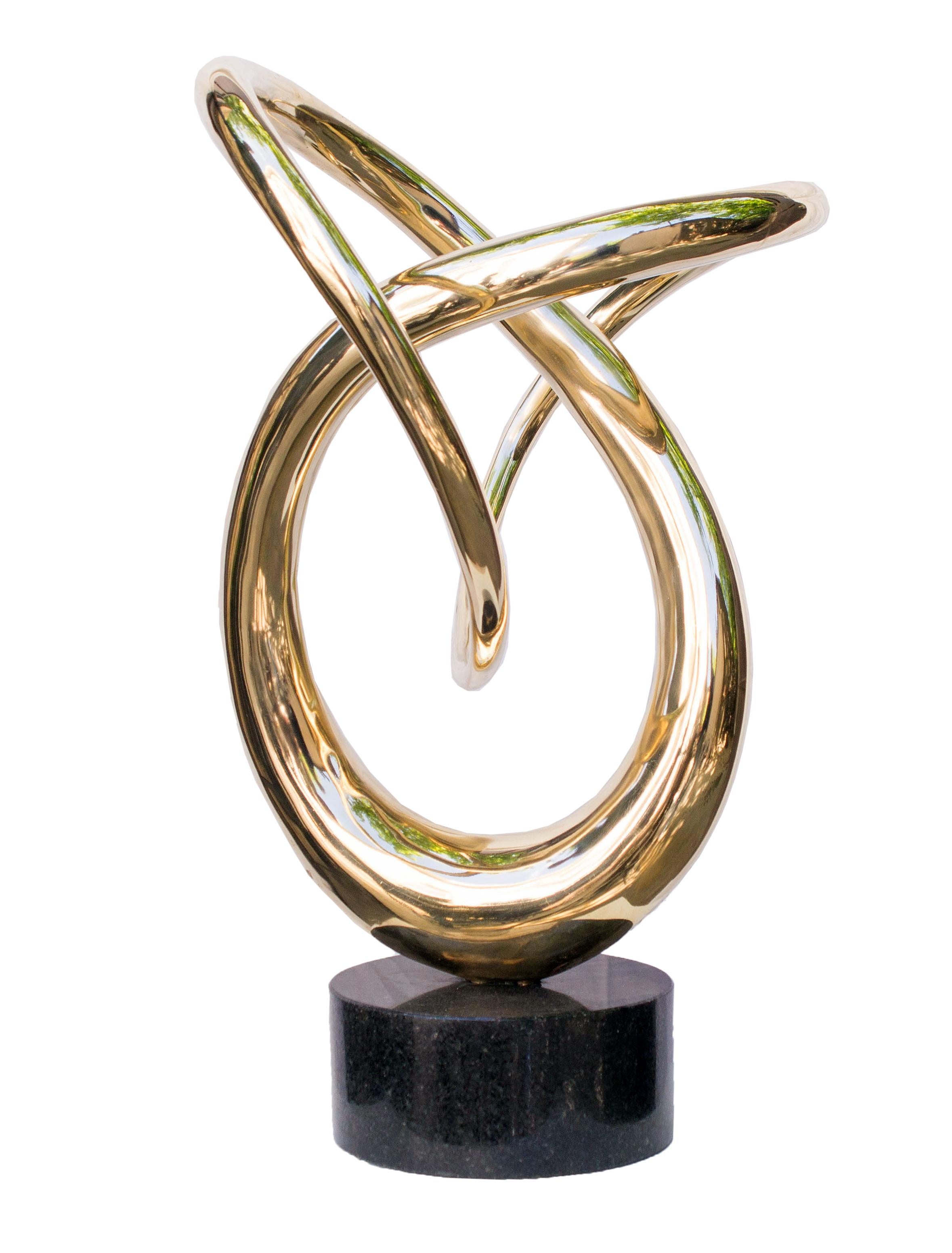 The shape of the sculpture is a complex intertwining of smooth, curved metal lines, resembling an abstract symbol of infinity. The mirror-like surface of the bronze reflects light, creating a dynamic visual effect. The base is made of dark granite,