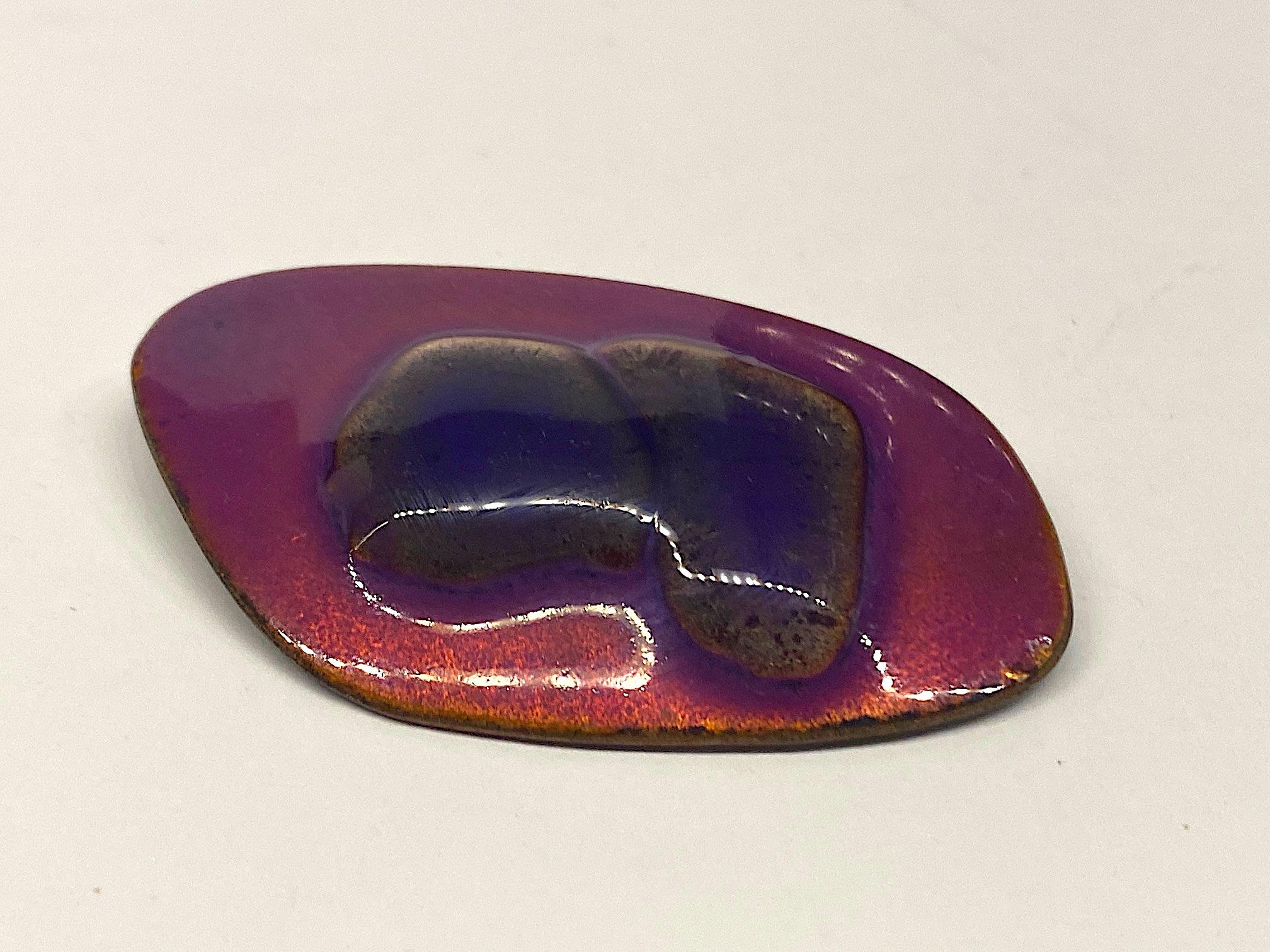 A lovely and colorful two tone purple enamel brooch from the 1960s by Kay Denning. The brooch is an asymmetric in shape and measures 2.5 inches ling and 1.38 inches tall. The enameling involves the use of heating the dark purple glass bits on the