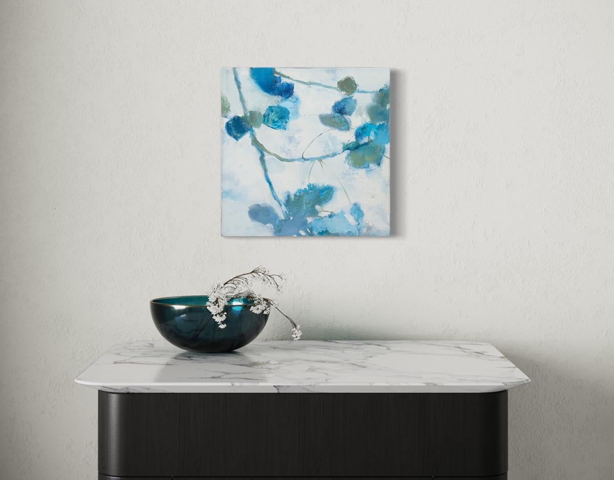 This small abstract floral painting by Kay Flierl is made with oil on canvas and features a cool blue and white palette with earthy green accents. Painted abstract botanical shapes fan from the top left corner down toward the bottom and right edges