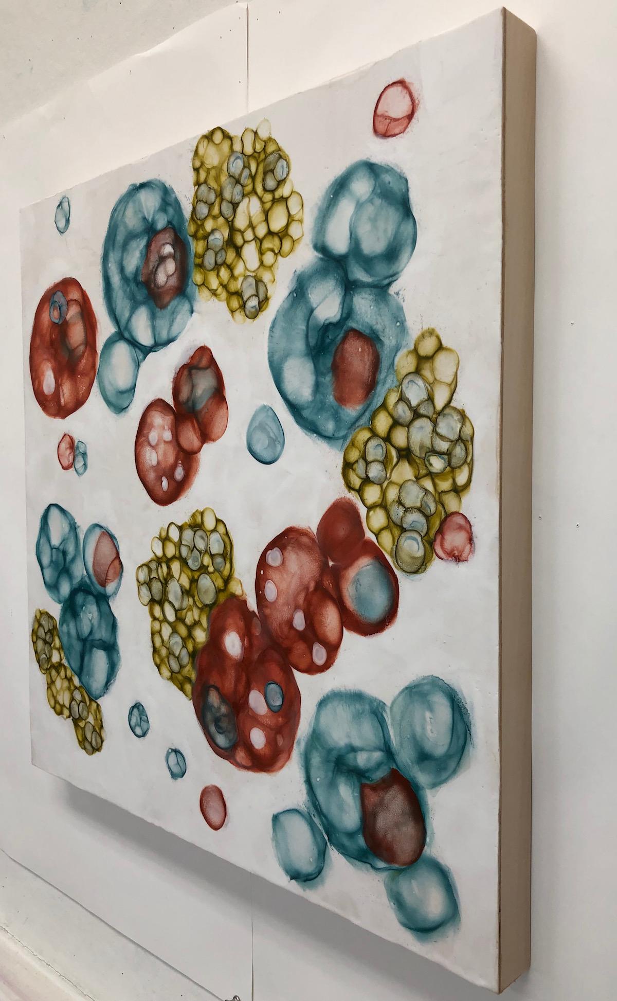 Kay Hartung’s “Bio Flow 23” is a 24 x 24 x 1.5 inch encaustic painting depicting floating microscopic forms. In colors of teal, rust, yellow green, and white, the composition creates a sense of the growth and movement of cells. The painting is