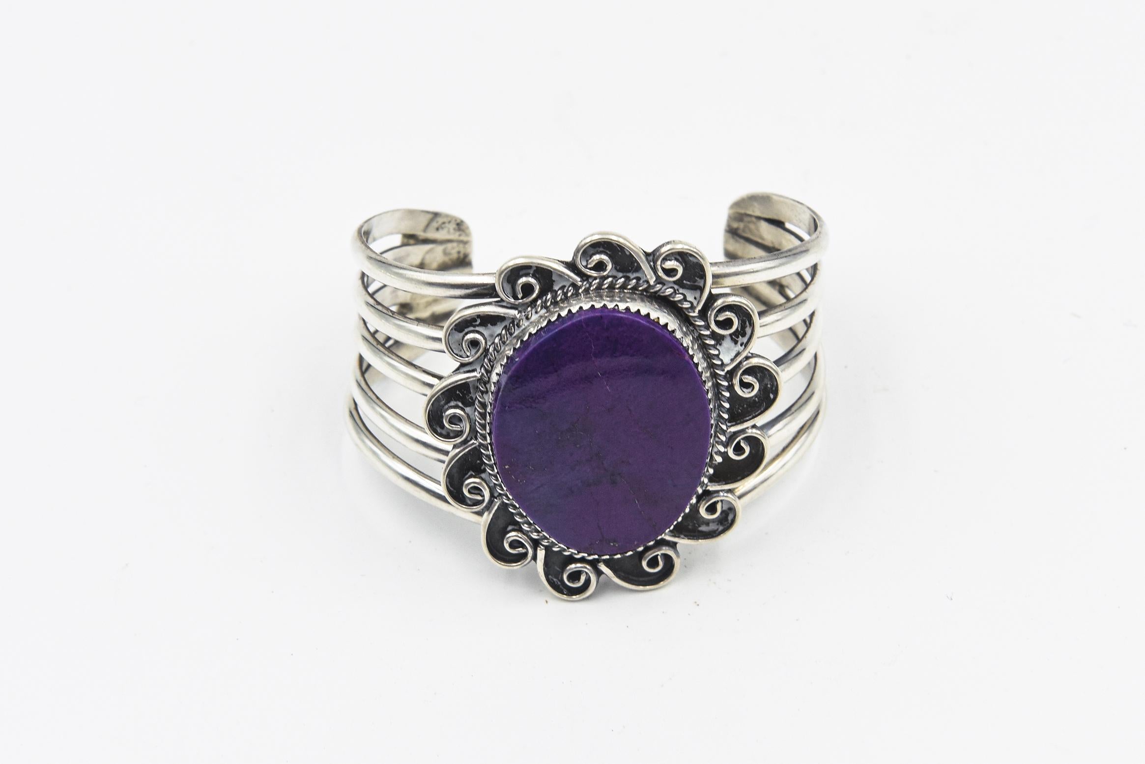 An impressive Navajo-inspired bracelet by Arizona silversmith Kay Johnson, the large oval sugilite is  set in a saw-tooth bezel and framed in sterling rope enhanced by thirteen hand-made scrolls that resemble either rays of sunshine or a flower.  It