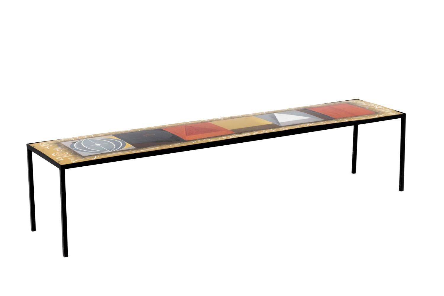 Kay Whitcomb, signed.

Rectangular coffee table in enameled metal standing on four square legs in black lacquered metal. Enameled tray figuring geometrical colored motifs and writings, white letters indicating “Emaillerie Crahait” are framing