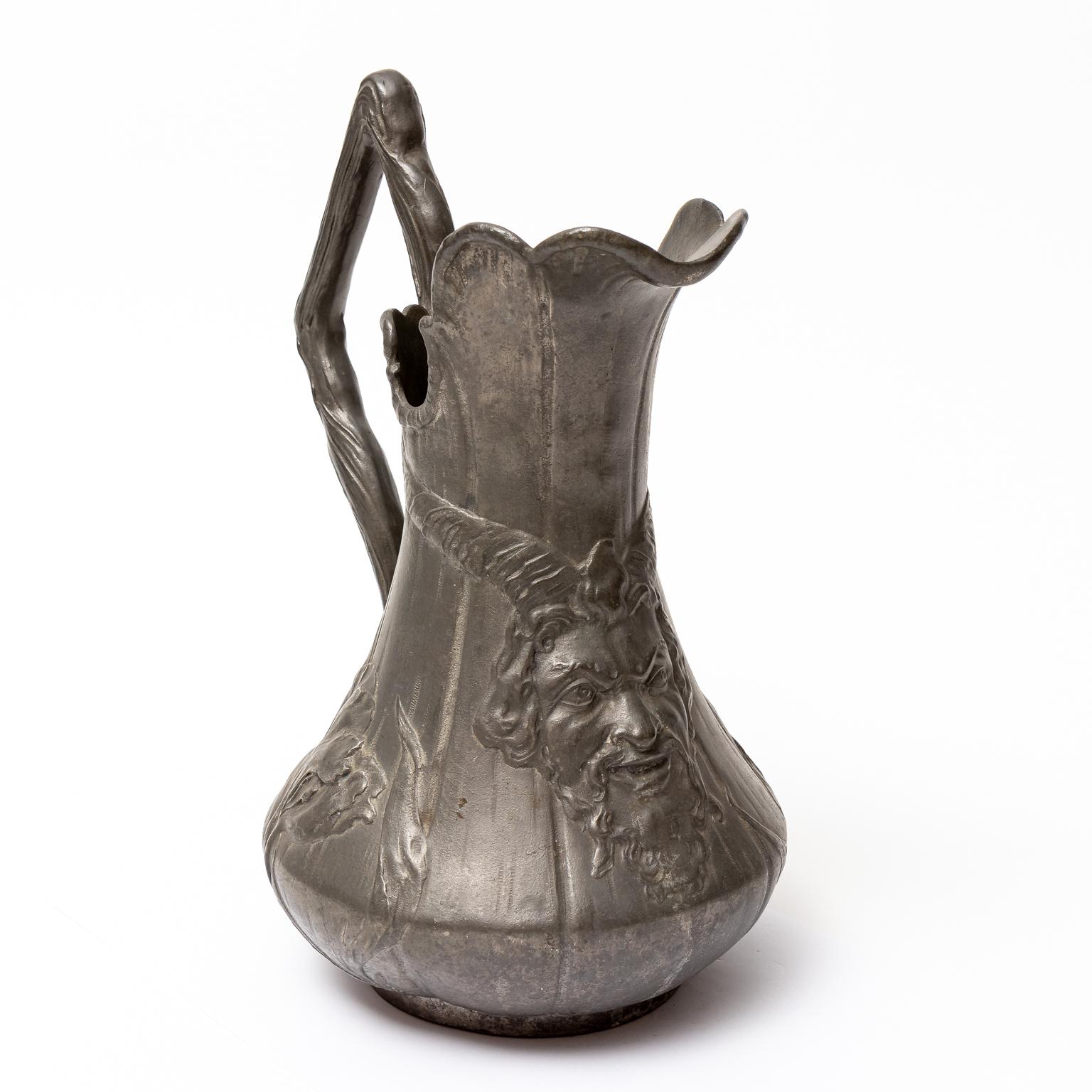 Circa 1900s large German Kayserzinn Art Nouveau style Pewter pitcher. The piece features an irregular ruffled lip, an angular handle. The body is decorated with irises and a Satyr. A maker's mark is impressed on the underside, No. 4061. Made in