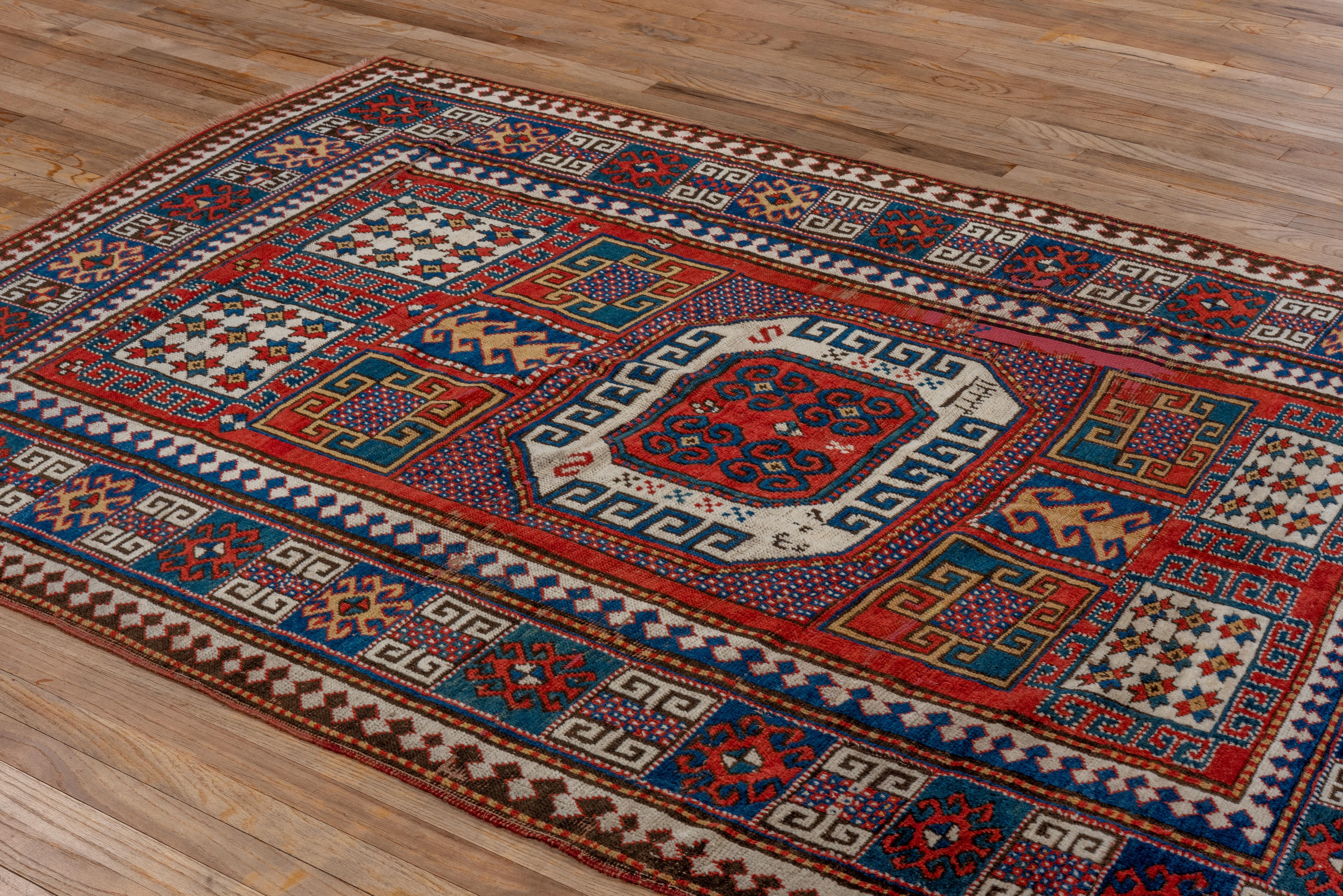 Vibrant and bold, this Kazak rug showcases a central ivory octagon medallion framed by richly saturated panels in cobalt, saffron, and crimson. The field features hooked motifs, stylized stars, and archaic border patterns. A spirited tribal