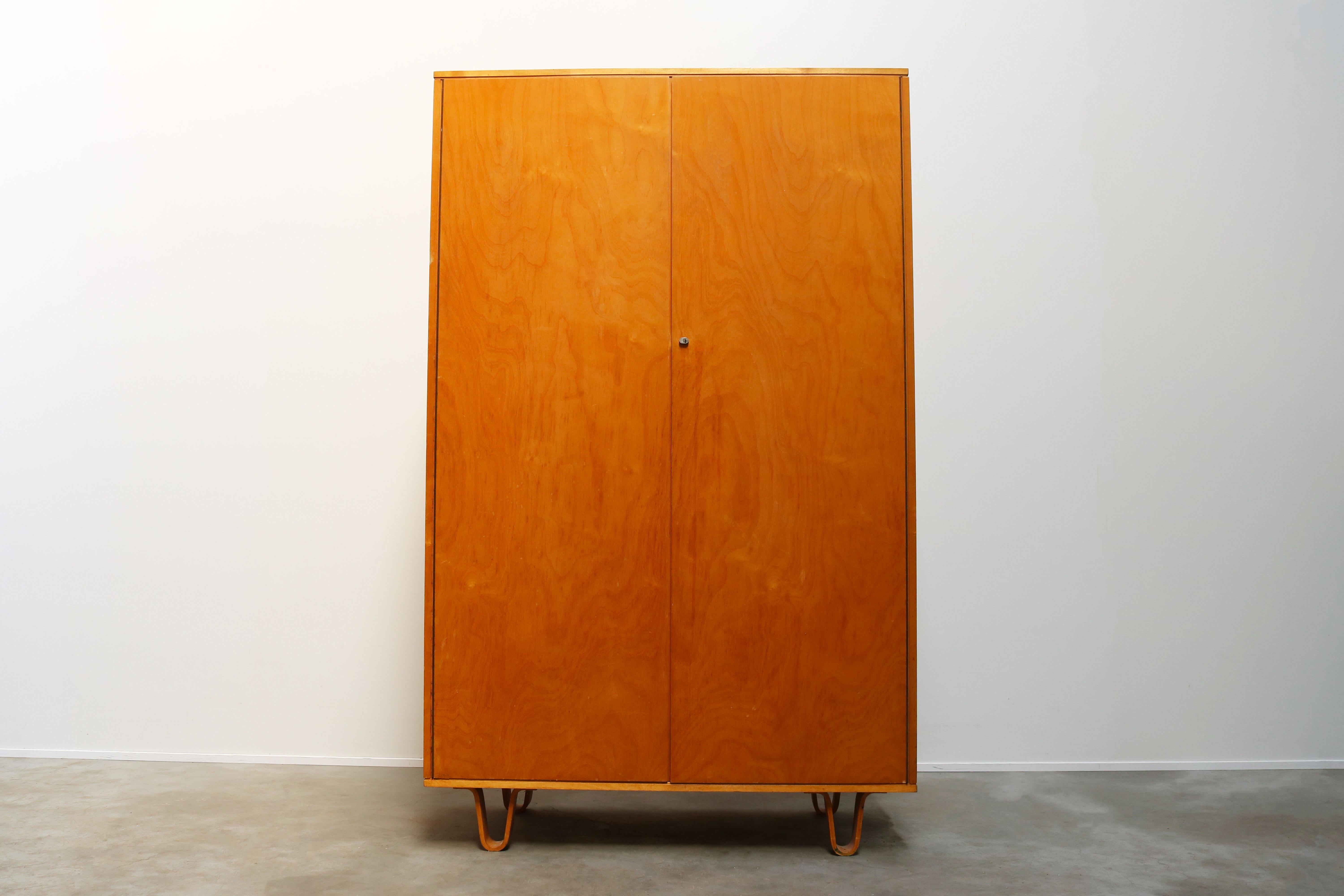 This KB03 cabinet is from the Birch series and was designed by Cees Braakman and produced by UMS Pastoe in the 1950s. It has distinctive laced feet. The cabinet has a wardrobe on the right and 4 shelves, small shelf and mirror on the left side.