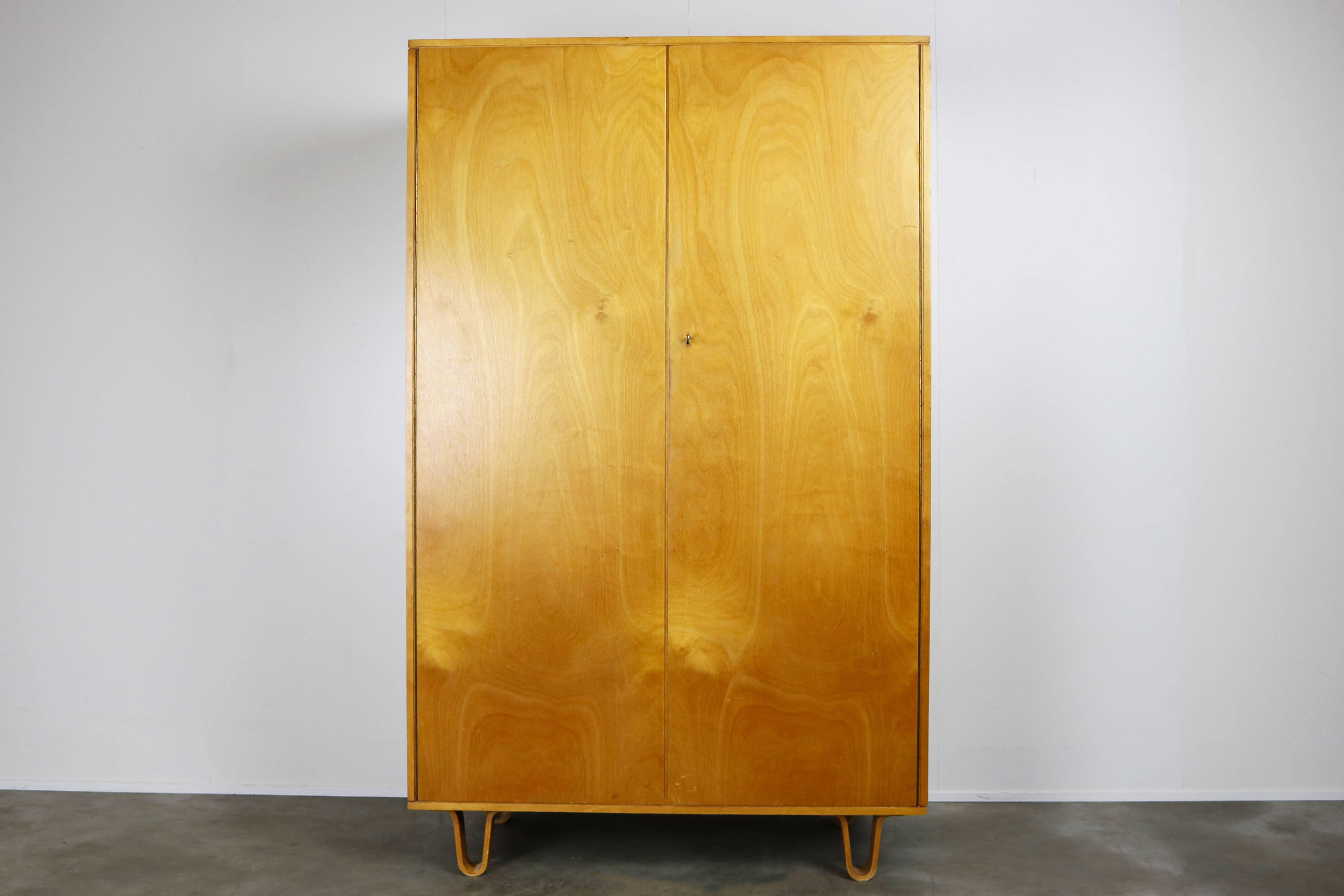 This KB03 cabinet is from the Birch series and was designed by Cees Braakman and produced by UMS Pastoe in the 1950s. It has distinctive laced feet. The cabinet has a wardrobe on the right and 4 shelves, small shelf and mirror on the left side.