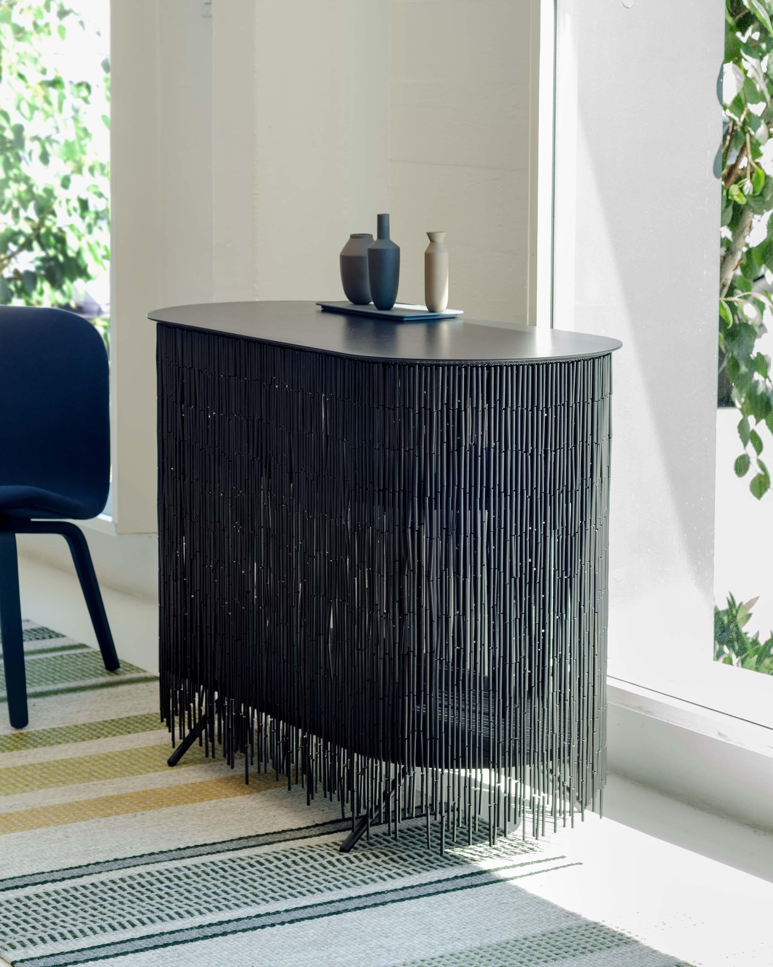 Keefer is a credenza that alludes to the objects stored within its shelves, yet obscures their identity through its bamboo-beaded skirt. The skirt masks the vertical supports, creating the illusion of floating shelves. The interior can be accessed