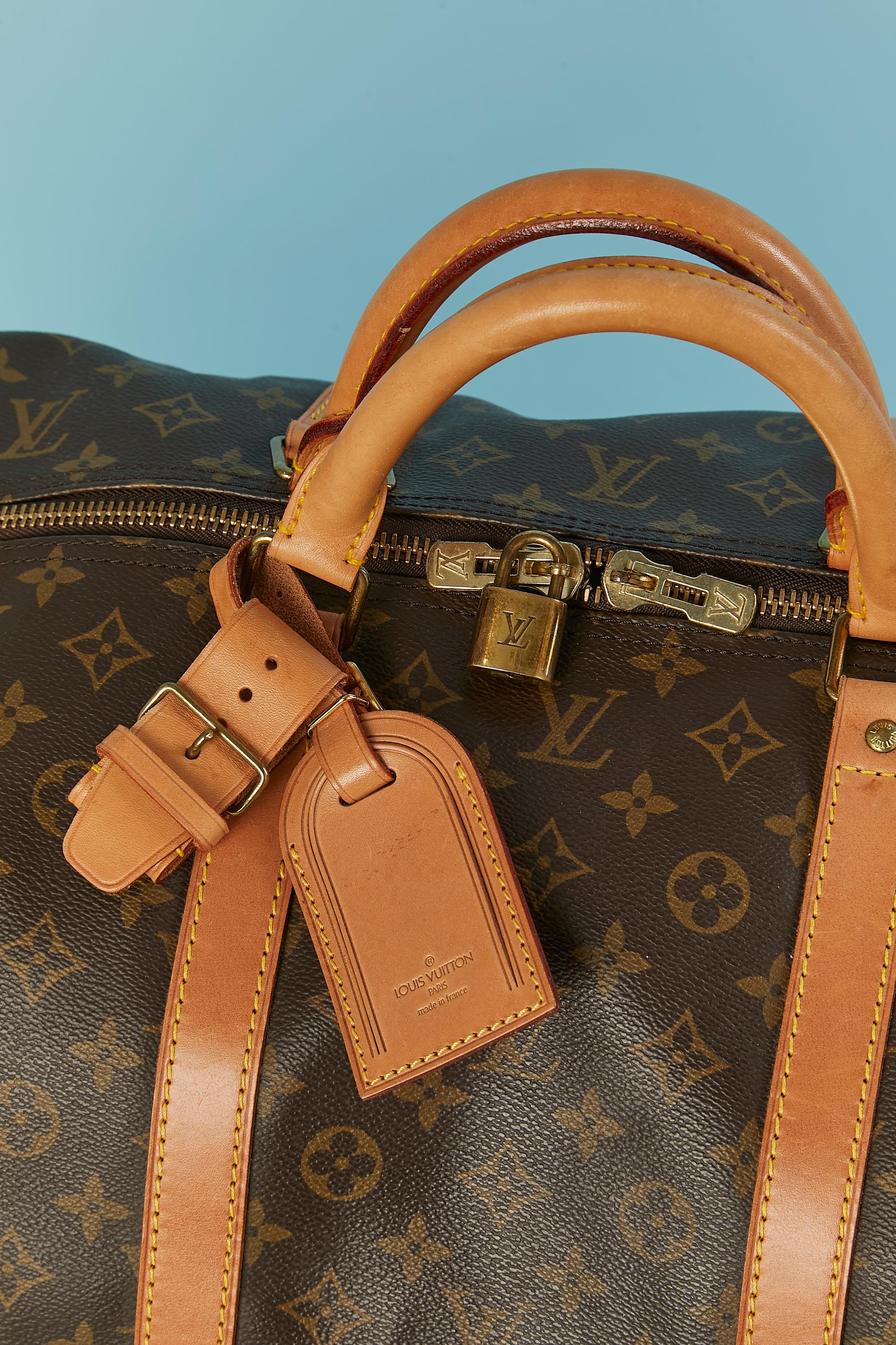 Keepall 60 Travel bag in leather with LV monogram print. 
Top zip closure. Brown cotton lining. Name tag in leather with extra short leather belt. No more shoulder-strap. Locker but no more key. 
SIZE : 60 CM X 33 cm X 26 cm 
