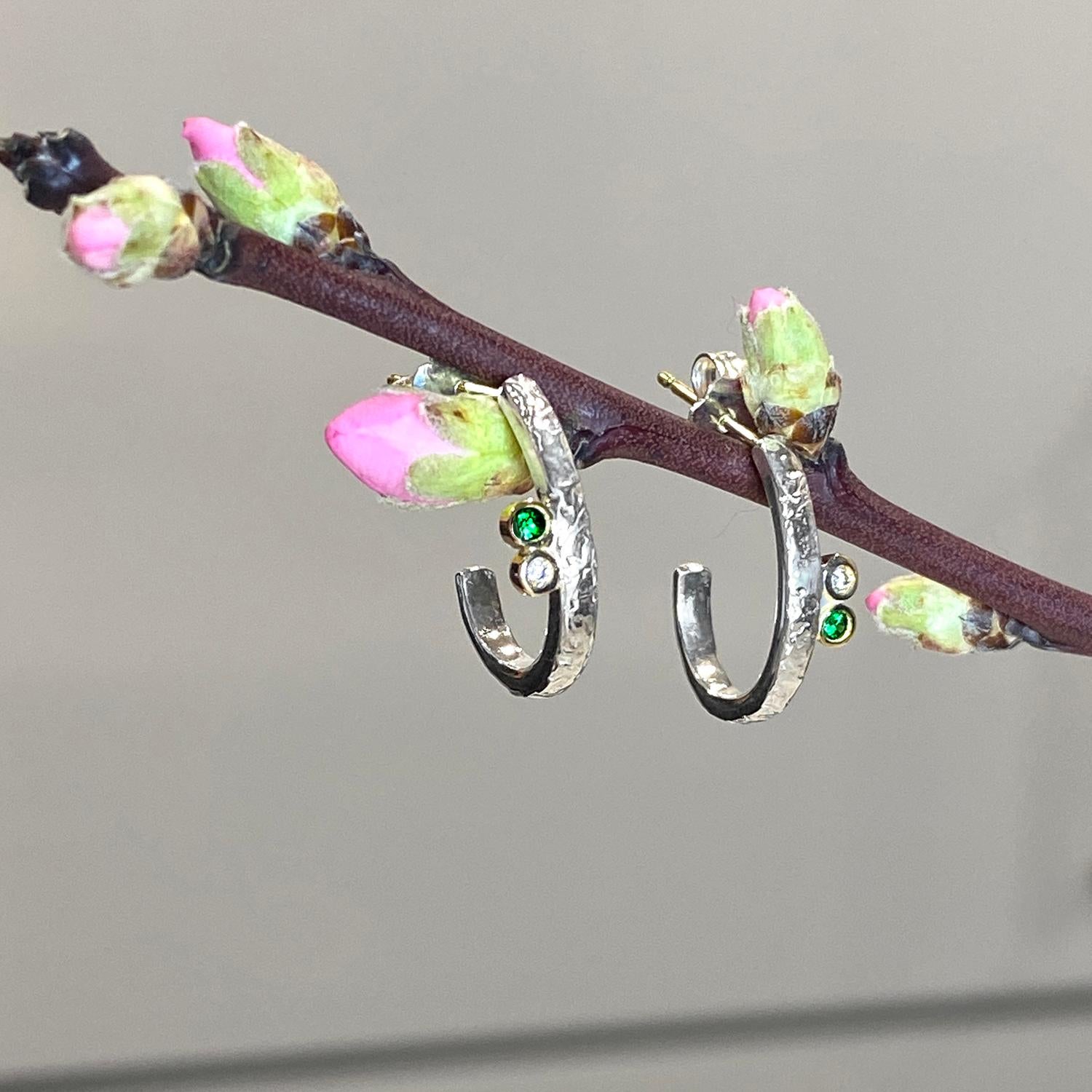Keiko Mita's contemporary Lyla Hoops are handmade from Sterling Silver and accented with 0.02 Carats Diamonds (total weight) and 0.06 Carats Green Garnets (total weight). The textured hoops have 14 Karat Gold posts with Sterling Silver post catches.