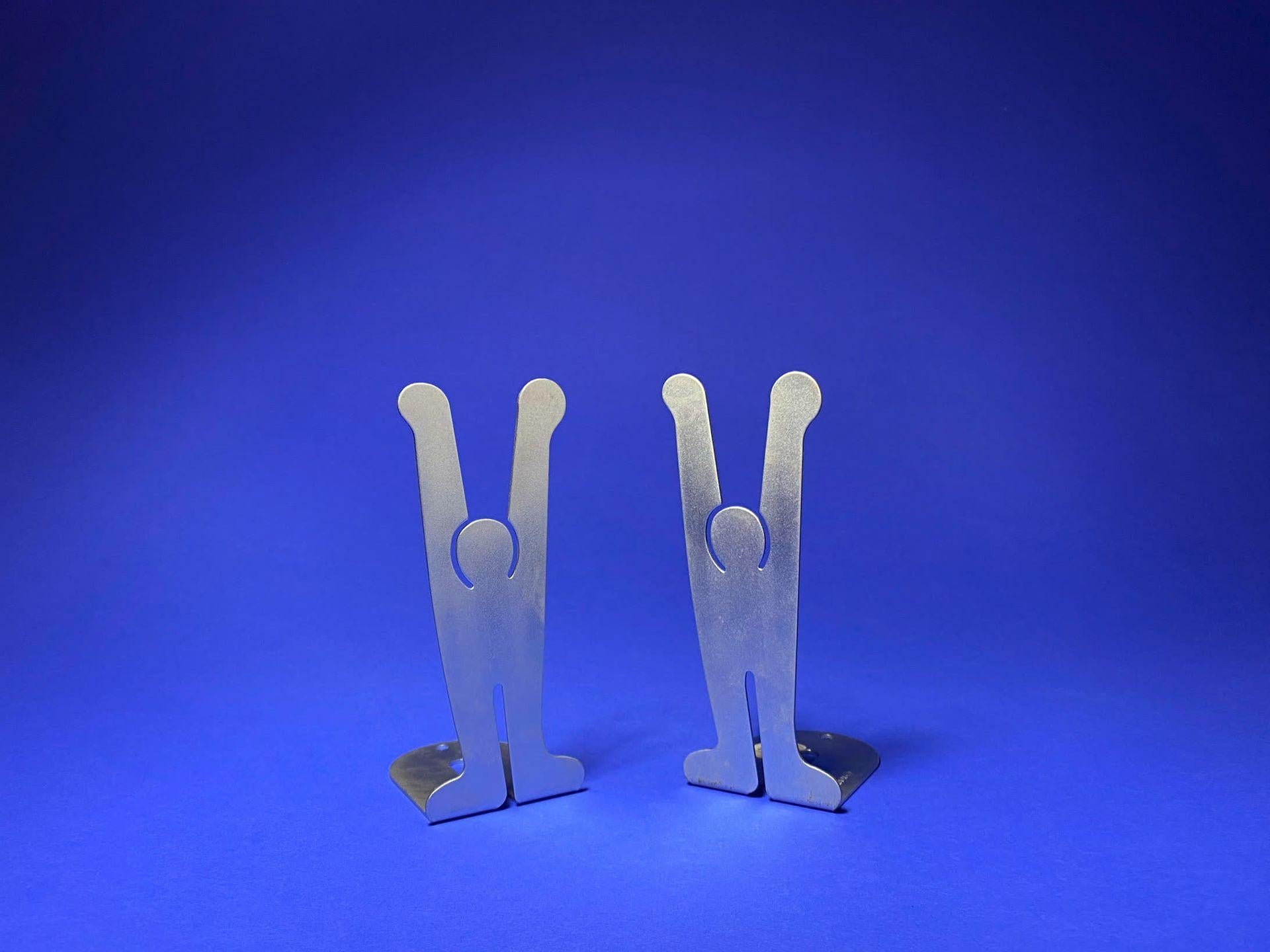 Silhouette mit erhobenen Armen, entworfen von Keith Harring, ein Paar Buchstützen aus gebürstetem Metall mit der Aufschrift Keith Harring.