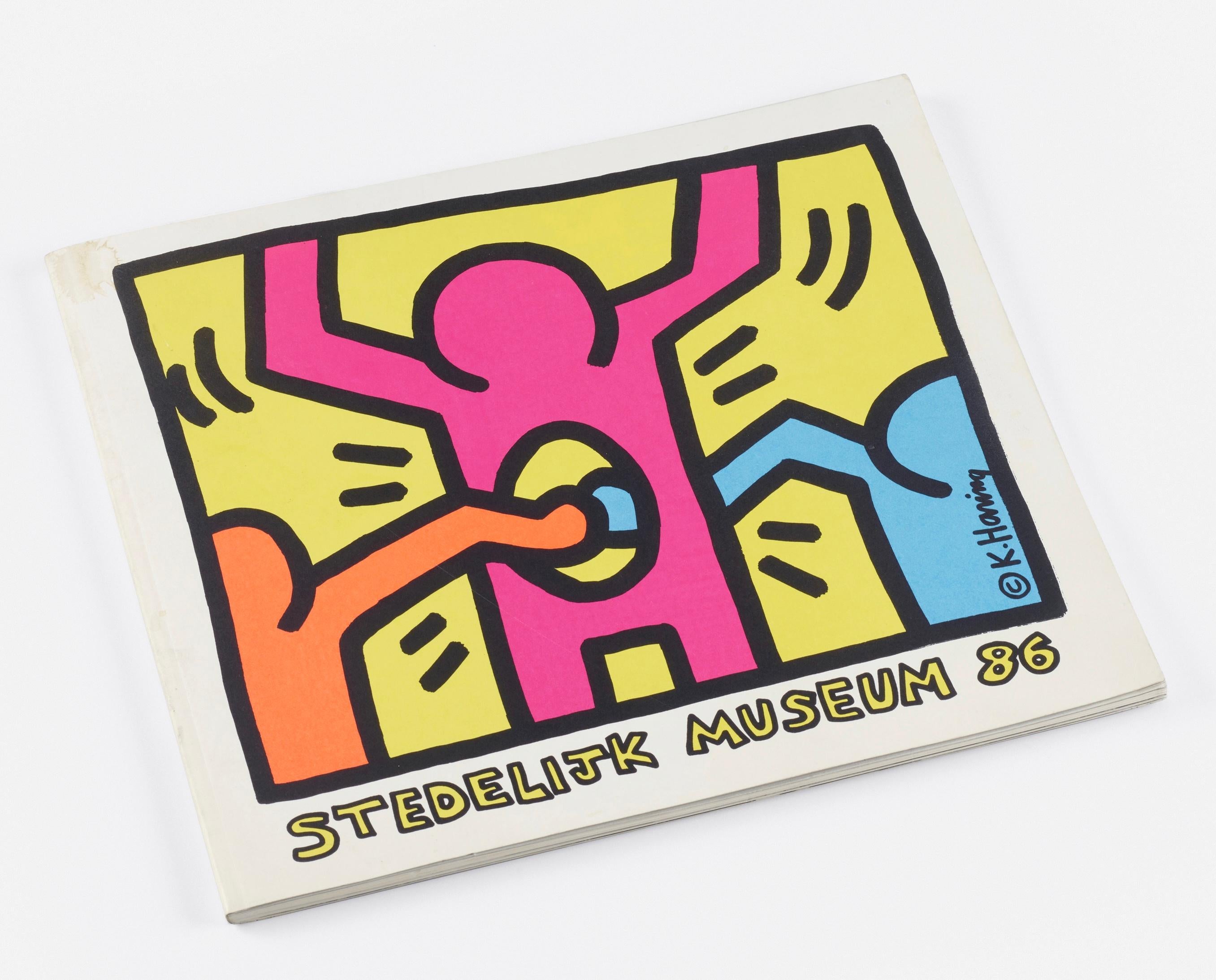 Keith Haring at the Stedelijk Museum, Amsterdam, Netherlands, March 15th – 12th May, 1986:
Signed Keith Haring Stedelijk Museum exhibition catalogue featuring a Keith Haring dancing man drawing connected to the artist's emblematic circle cross. To