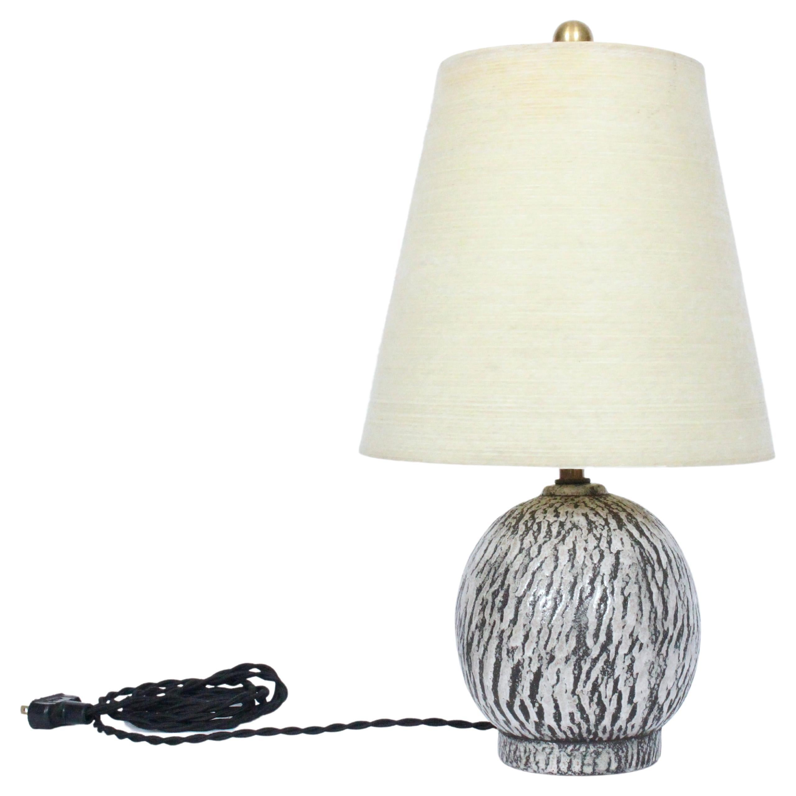 Petite American Organic Modern volcanic like glazed Table Lamp by Kelby. Featuring a handcrafted globe form, textured bark like glazed surface, with Dark Charcoal and tan speckled thick Off White coloration. 10.5 H to top of socket. Shade shown for