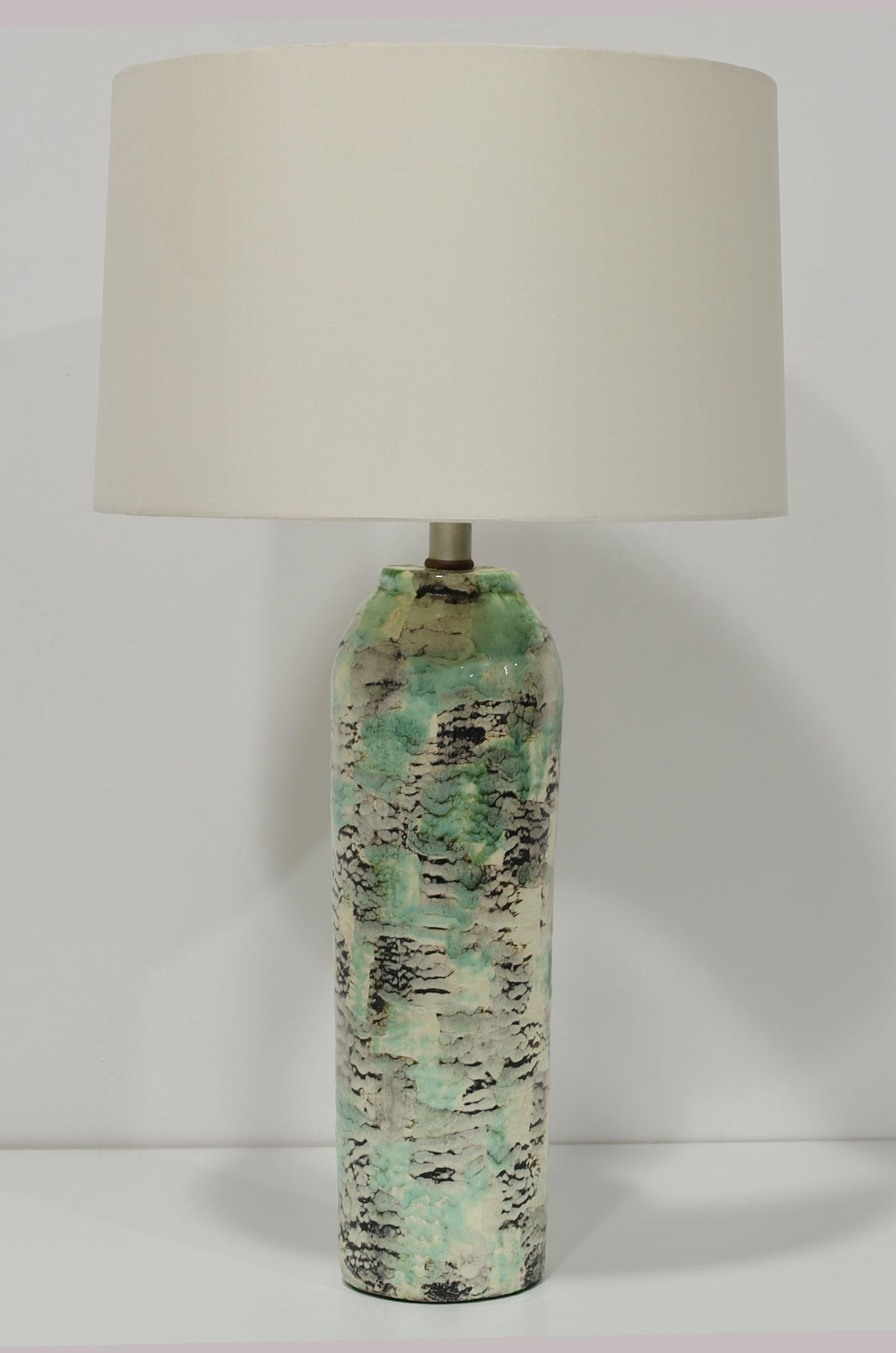 This is a unique lamp by Kelby. The lamp is circular drum shape with an abstract design in greens, black and cream or off-white. The ceramic height is 17.5