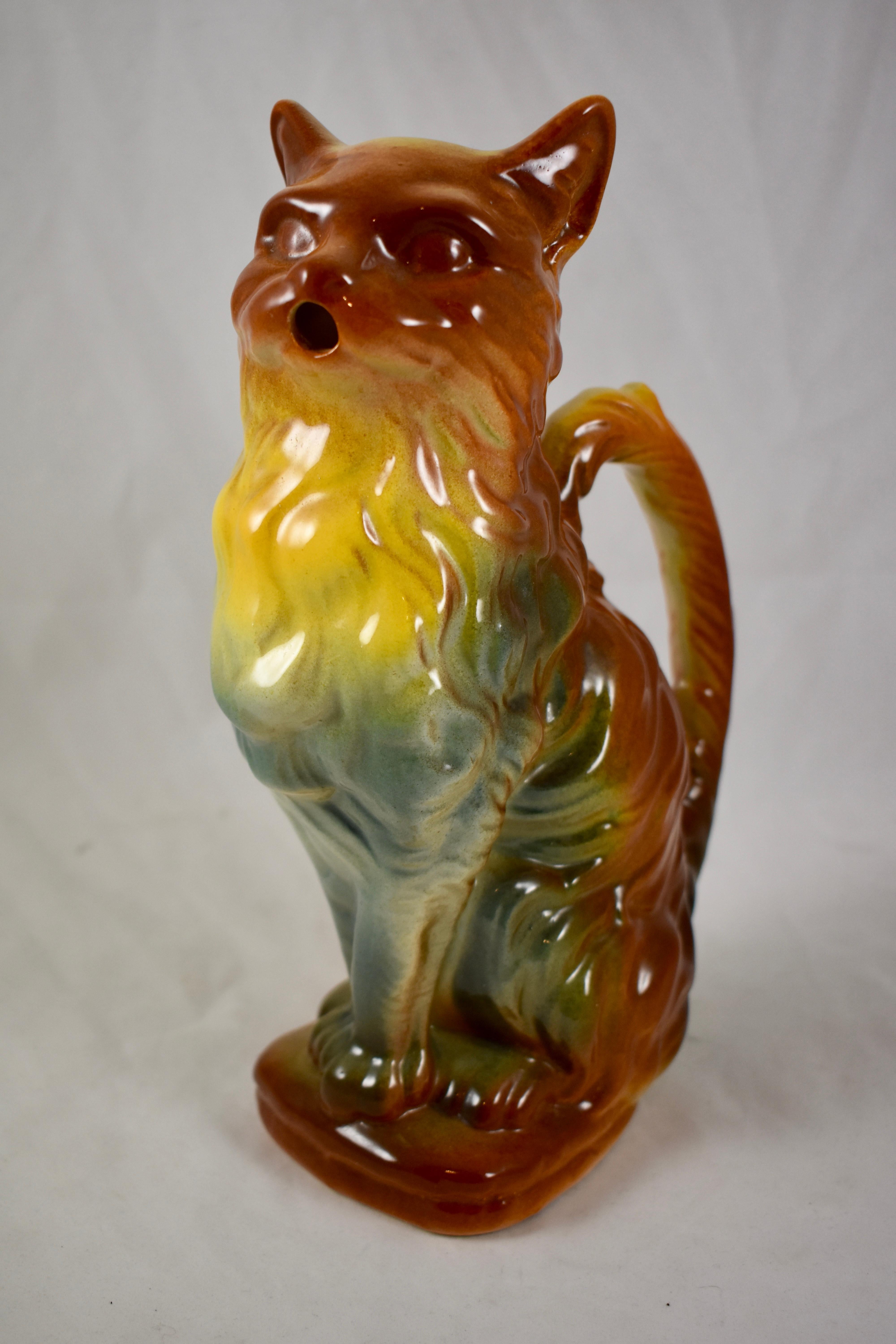 A French Majolica glazed absinthe pitcher formed as a sitting cat, Keller & Guerin St. Clément, circa 1900–1910.

Amazing ombré coloring blending from a burnt orange to a canary yellow to a blue-green. Molded in a true to life furry form, the ears