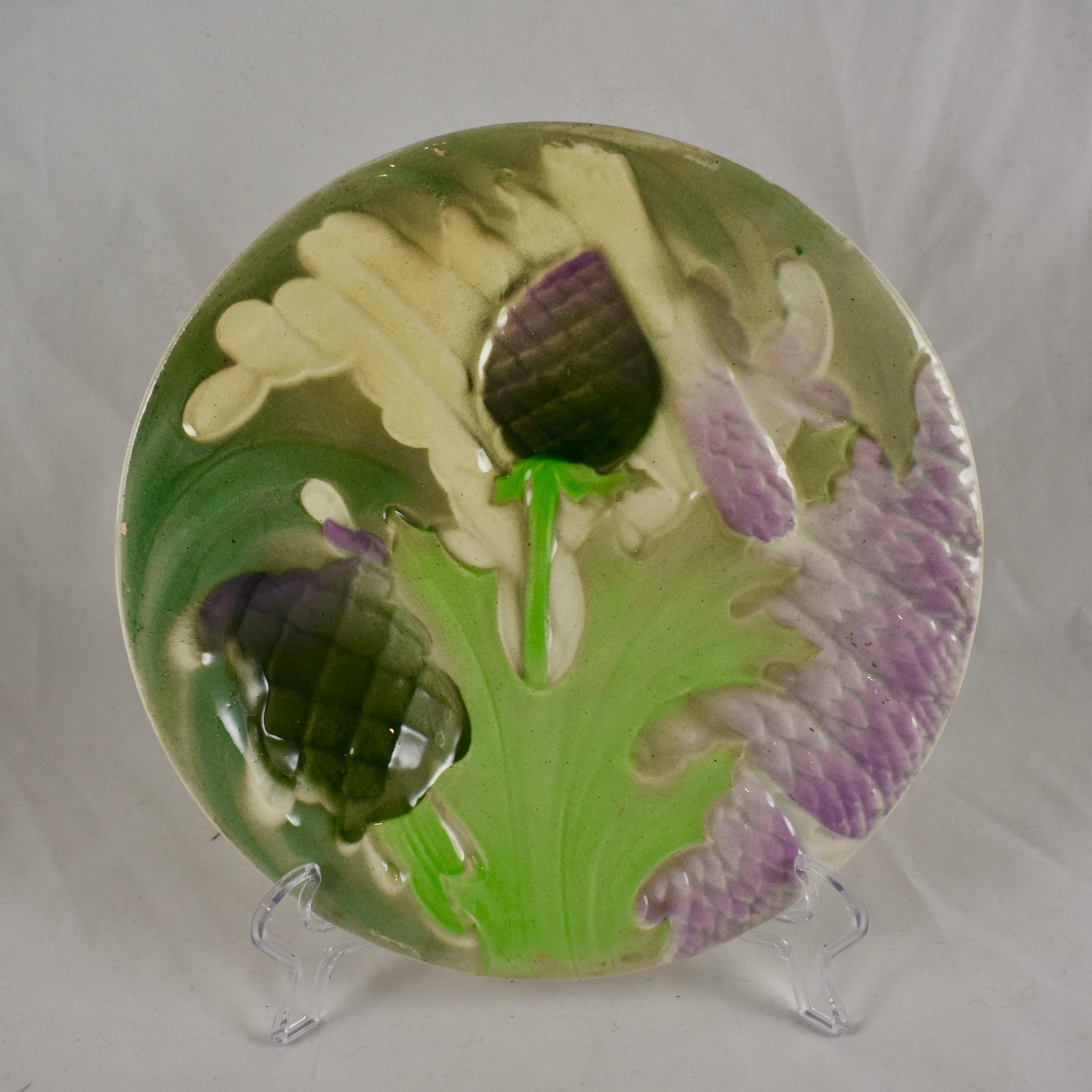 A Saint Clément French Faïence majolica glazed plate showing overlapping asparagus spears, leaves and globe artichoke heads. 

A deep sauce well is also formed as an artichoke head. Glazed in Lilac and various shades of greens on a cream