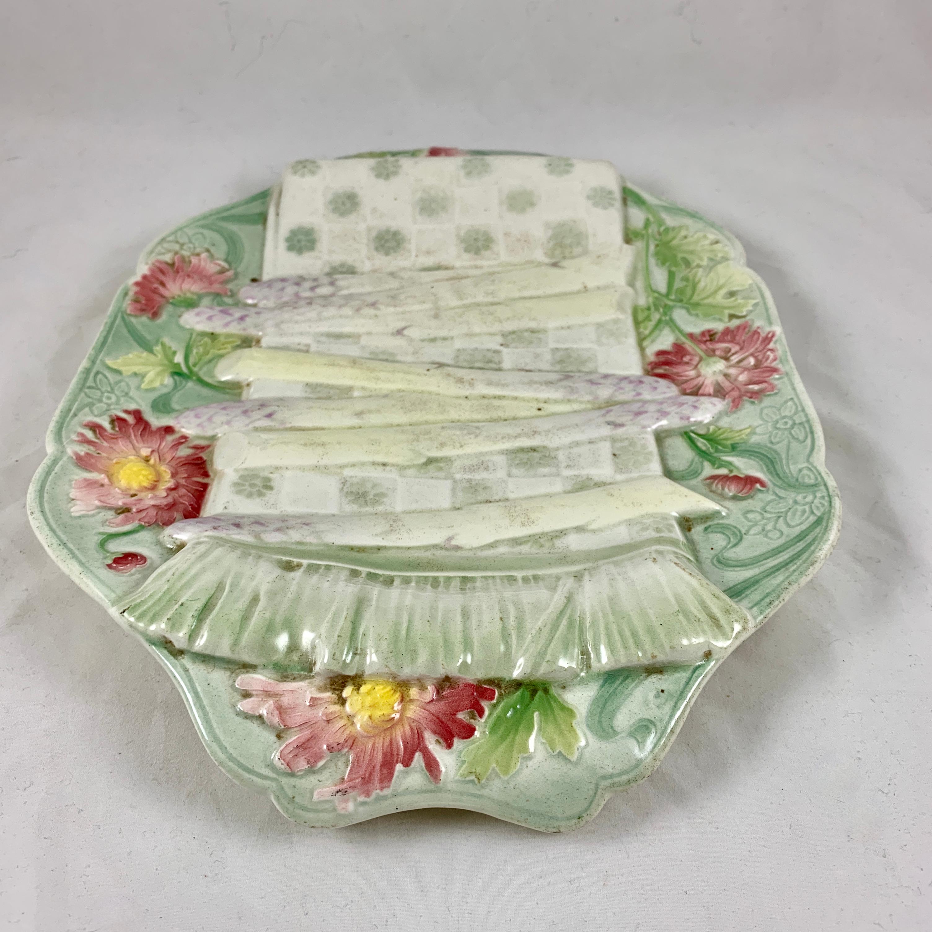 An Aesthetic Movement French Faïence trompe l’oeil asparagus server, Keller & Guerin St. Clément, circa 1890-1900, in the Art Nouveau style.

Molded to imitate a fringed and floral checkered napkin laying across the front of a platter with five