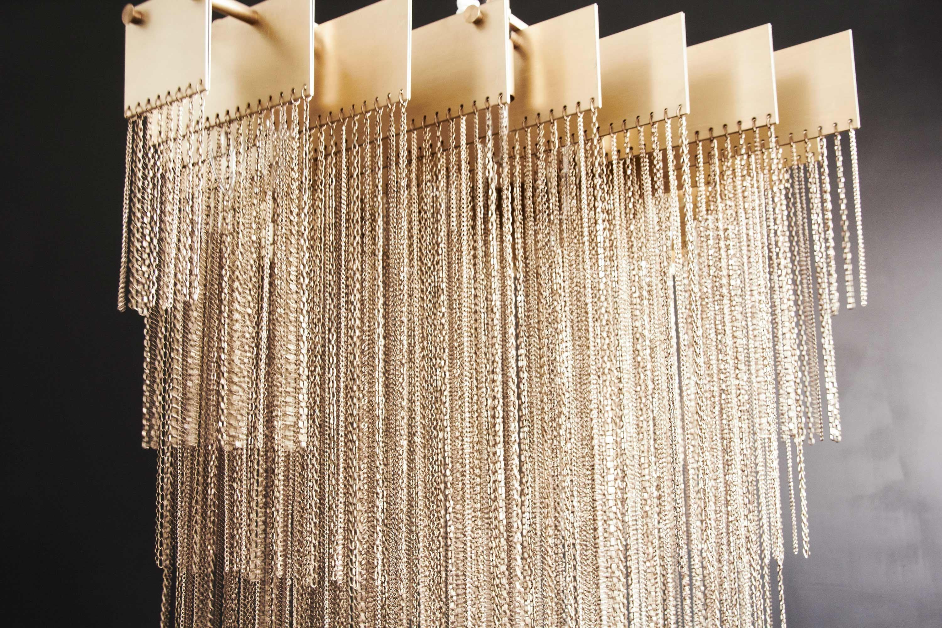 The Kelly chandelier by Gabriel Scott has metallic blades, carrying a half-kilometer of various metallic chains which are symmetrically gathered in an ascending form to create a sculpted geometric mass of glimmering light.