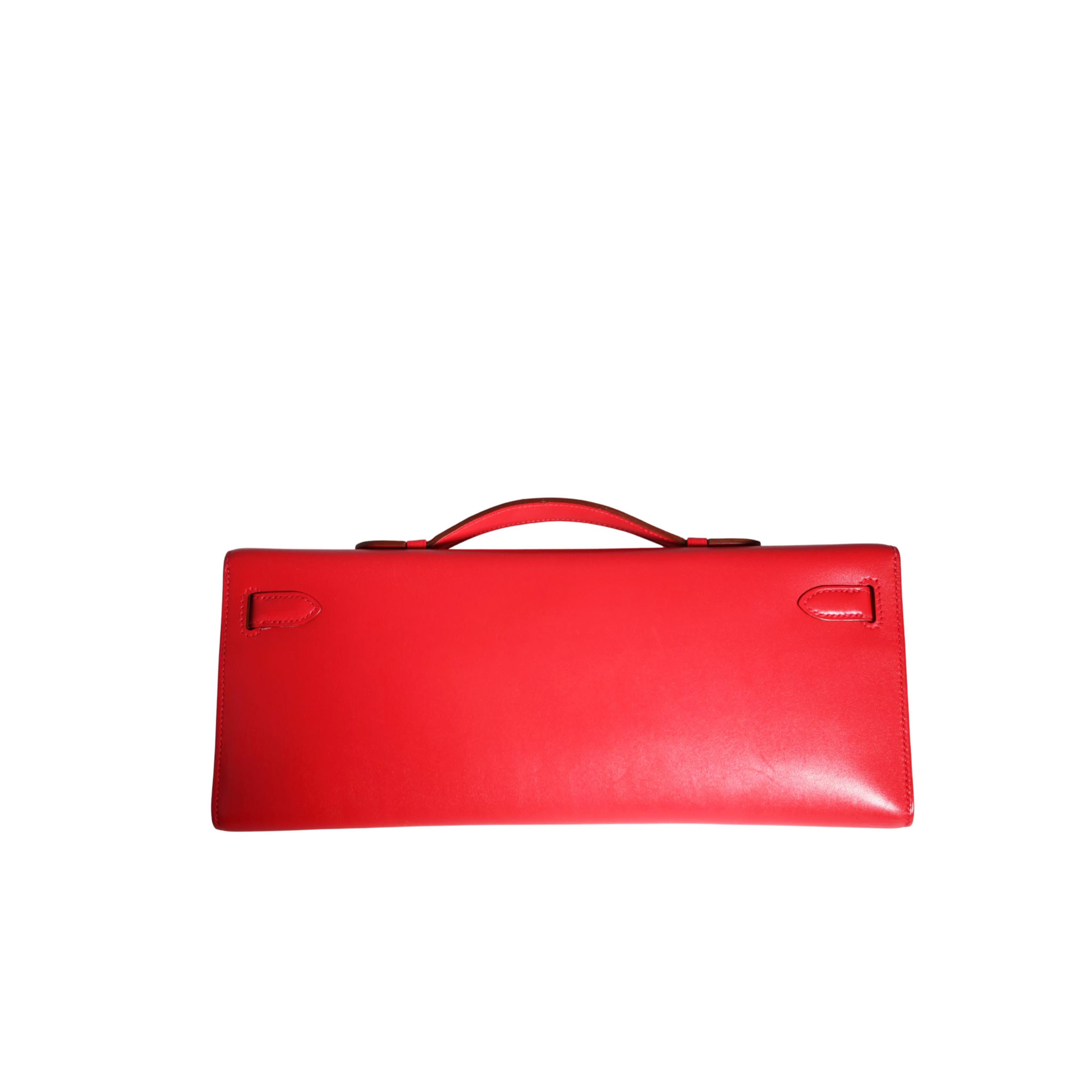Diese exquisite rotfarbene Kelly Cut Clutch Bag aus schnellem Leder ist mit farblich abgestimmten Nähten, Riemen an der Vorderseite und einem flachen Henkel an der Oberseite ausgestattet. Der Knebelverschluss wird durch silberne Palladiumbeschläge
