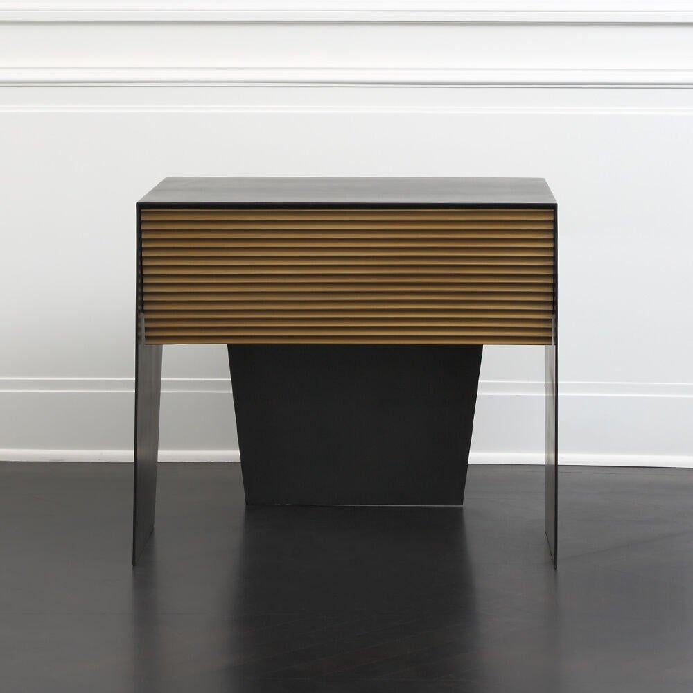 An incredibly modern and chic nightstand the Gallant is enclosed in solid stainless steel with a rich blackened patina. The single drawer in Ebonized Walnut features a linen lining, soft close glides, and a delicate scalloped bronze drawer front.