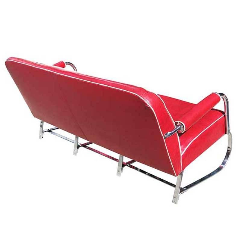 Un canapé en fer plat chromé conçu par Kem Weber, avec une base à ressorts courbée et les bras roulés emblématiques de Weber. Les bras sont surmontés d'accoudoirs en vinyle rembourrés rouges qui suivent la courbure du design du canapé. Il s'agit