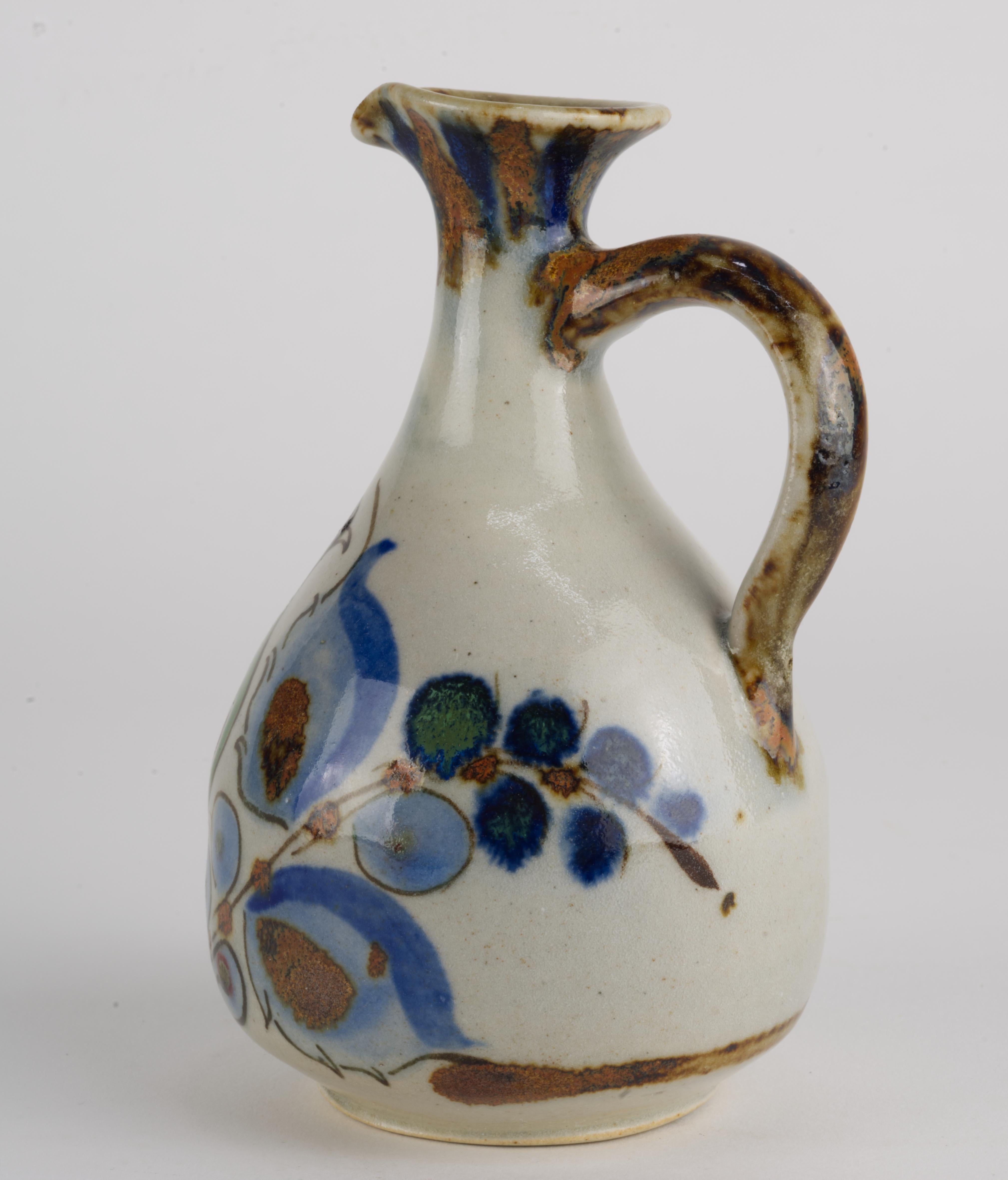  Ce vase vintage en forme d'aiguière a été réalisé à la main par Ken Edwards dans la tradition de la poterie Tonala. Il est décoré d'un oiseau et de fleurs abstraites dans une palette de bleu, de vert et de marron sur un fond gris doux.
