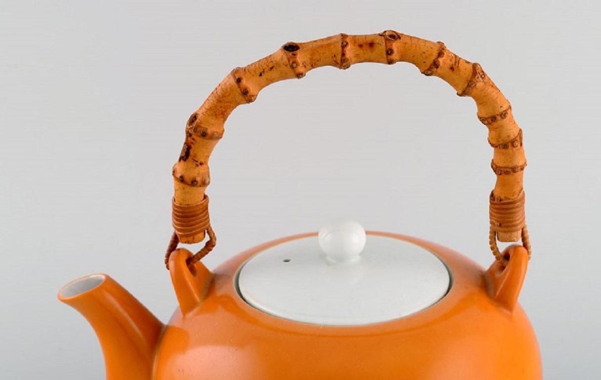 Kenji Fujita for Tackett Associates. Porcelain teapot with a bamboo handle. 
Beautiful orange glaze. Dated 1953-56.
Measures: 23 x 21 cm (incl. handle)
In excellent condition.
Stamped.