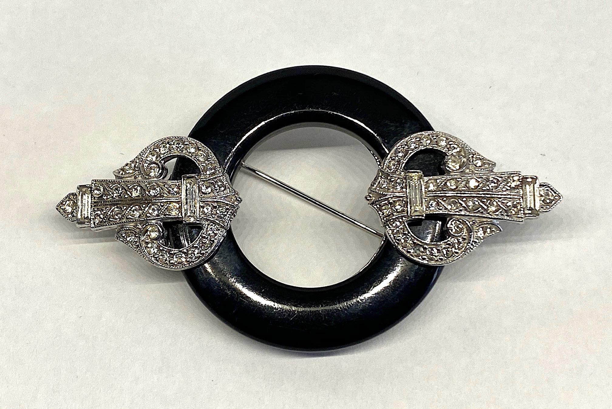A wonderful Art Deco style brooch in rhodium plate set with rhinestones and a black resin ring by the iconic fashion jewelry company Kenneth Jay Lane. The brooch is circa 1980 when  the desire and revival for all things Art Deco became popular. The