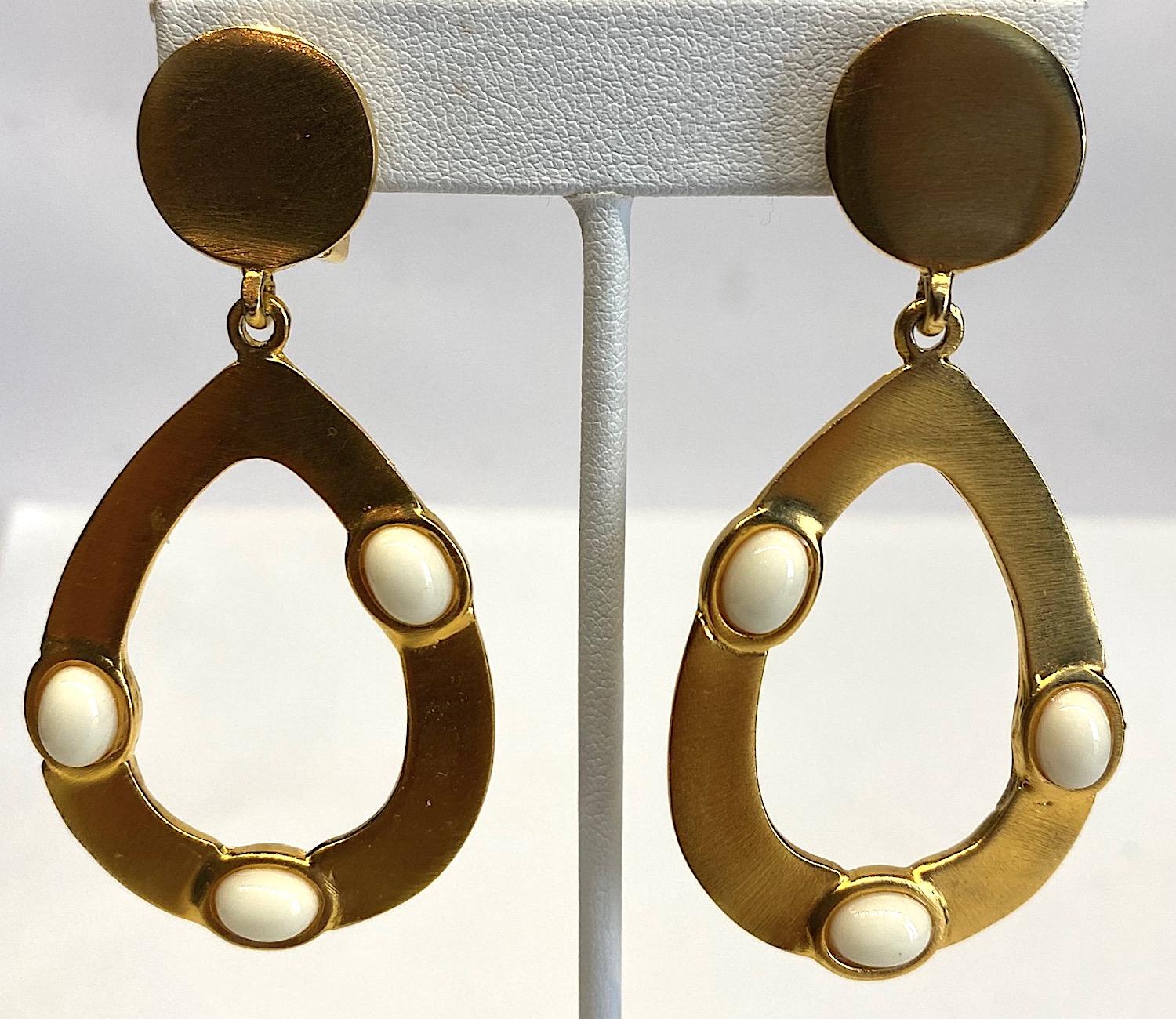 Kenneth Lane 1980s satin gold tone pear shape pendant hoop earrings with oval white cabochons. Each earring is 1.38 inches wide and 2.75 inches long. The top round button has a clip back and measures .63 of an inch in diameter. The pear shape