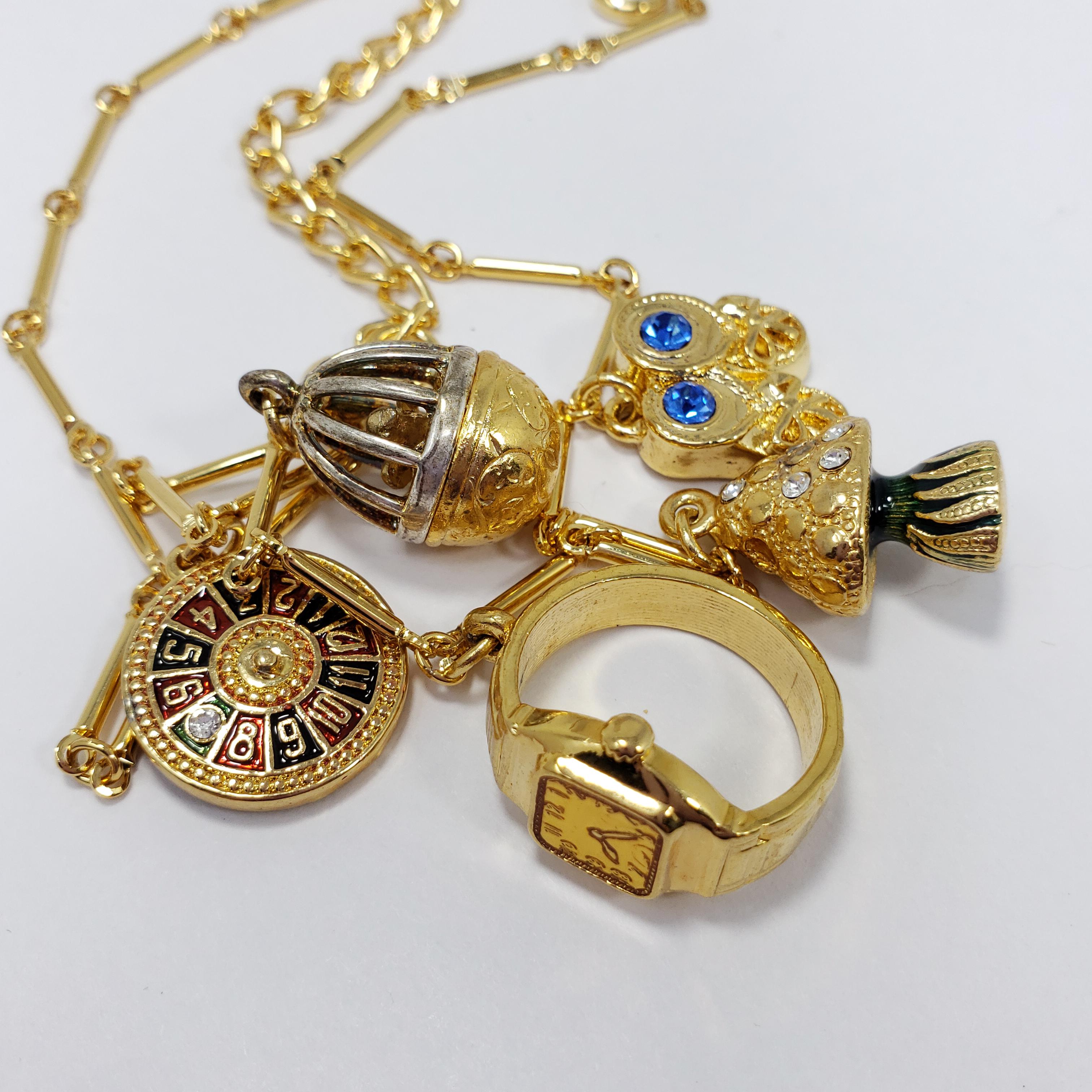 A quirky necklace by Kenneth Jay Lane. Features five charms - a roulette wheel, a birdcage, a ring, a tree, and a pair of shoes. Motifs are decorated with subtle crystal and enamel accents. 

Hallmarks: Kenneth © Lane
43.5cm plus 7.5cm extension